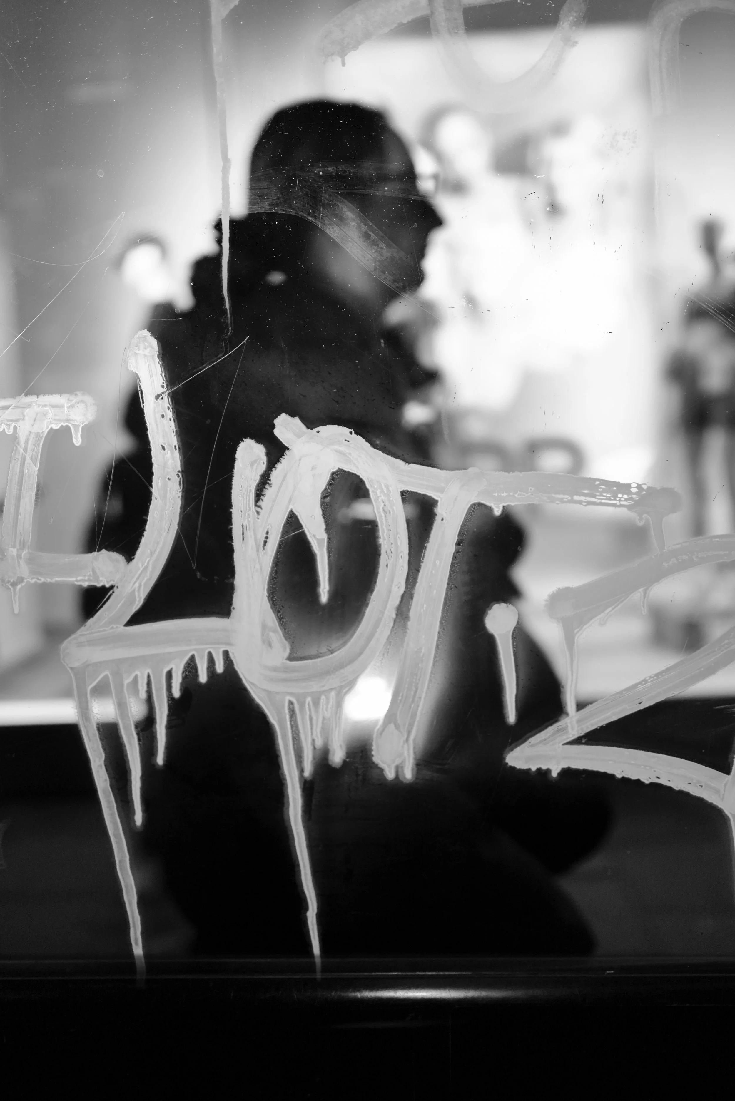 A black and white photo of a person reflected in a glass window with the words 'Happy New Year' written in white paint on the window.