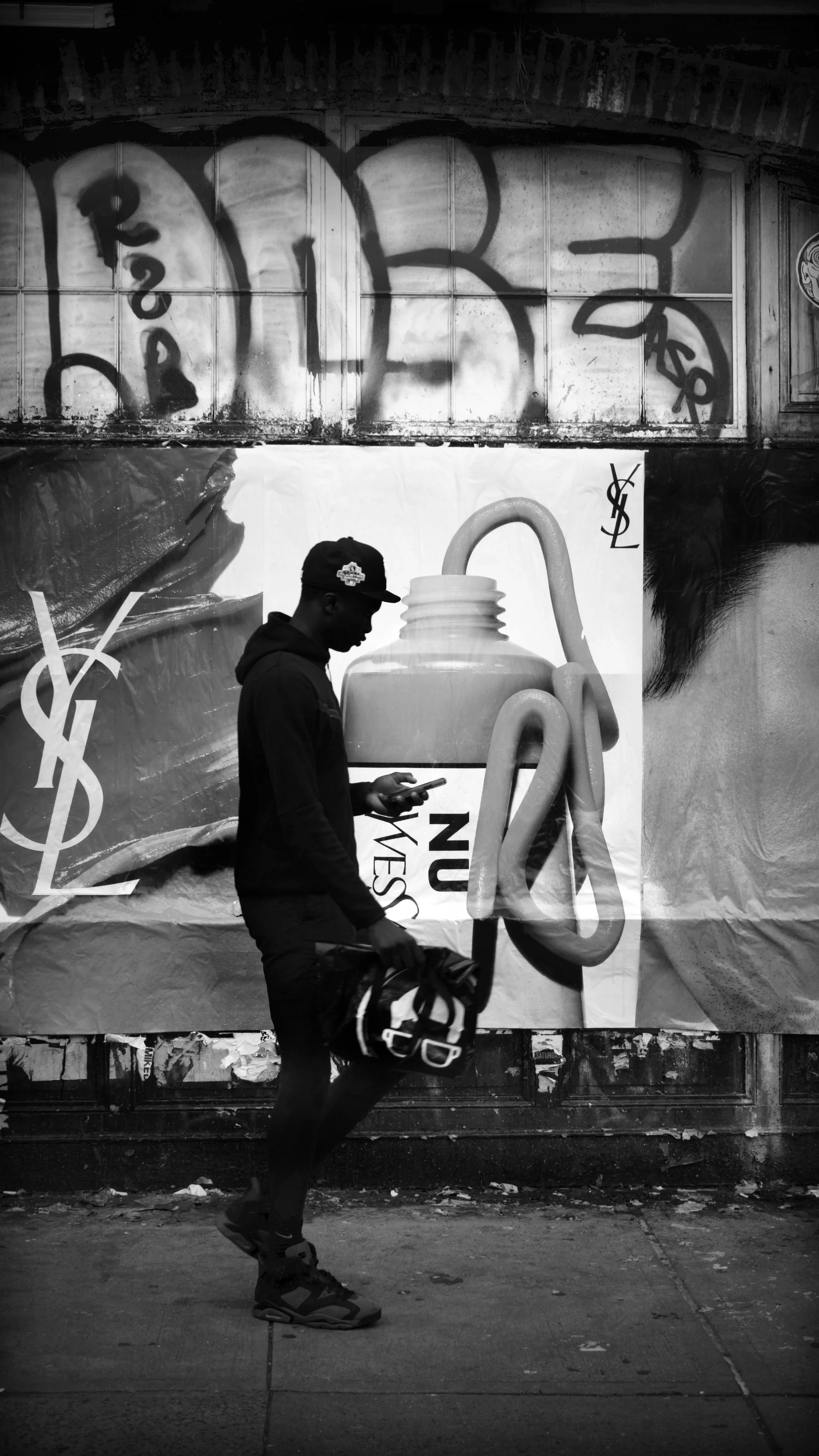 A silhouette of a person walking on the street with a phone in hand, carrying a bag, and a large advertisement billboard in the background.