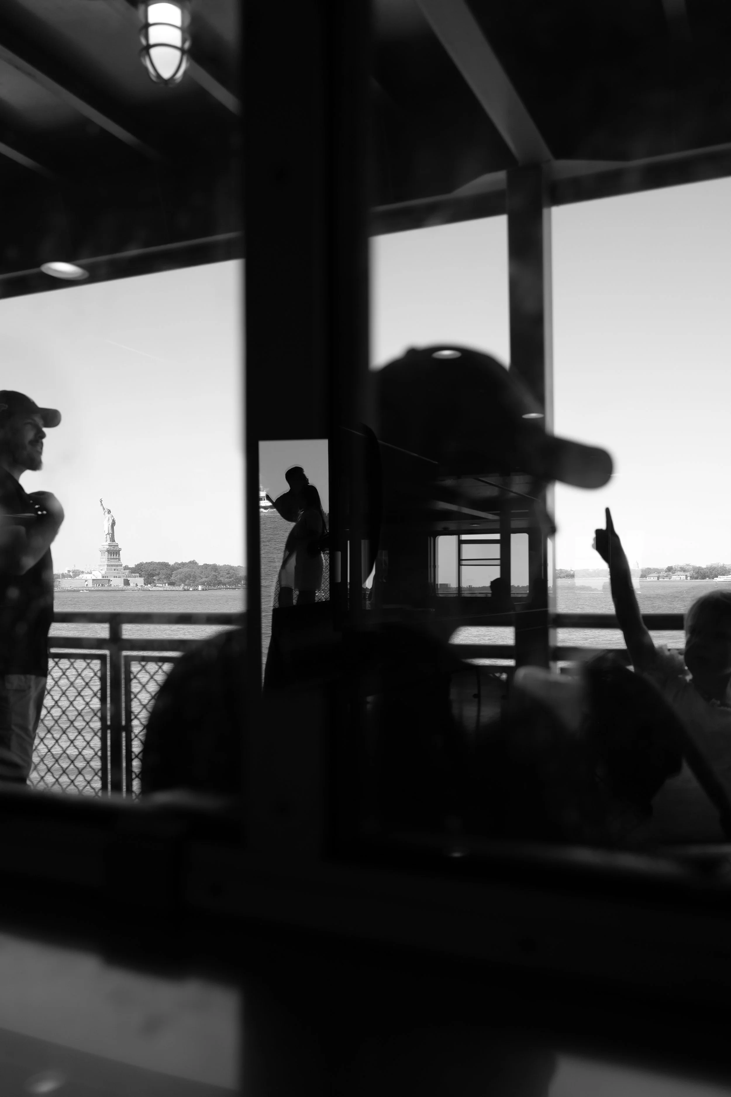 Silhouettes of people on a boat with the Statue of Liberty visible in the background, viewed through a window, black and white photo.