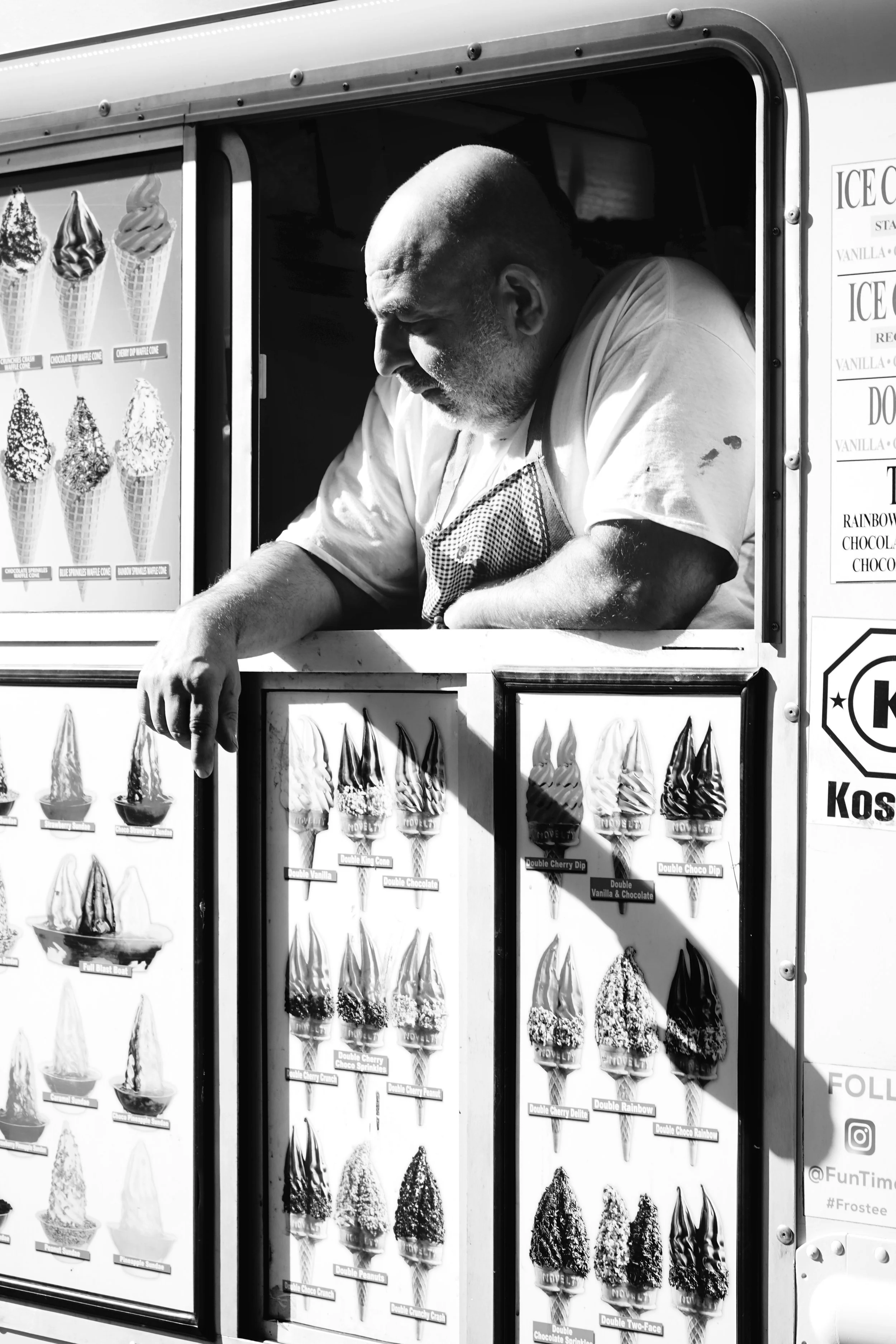 A man working at an ice cream truck serving customers, with images of various ice cream cones displayed on the truck.