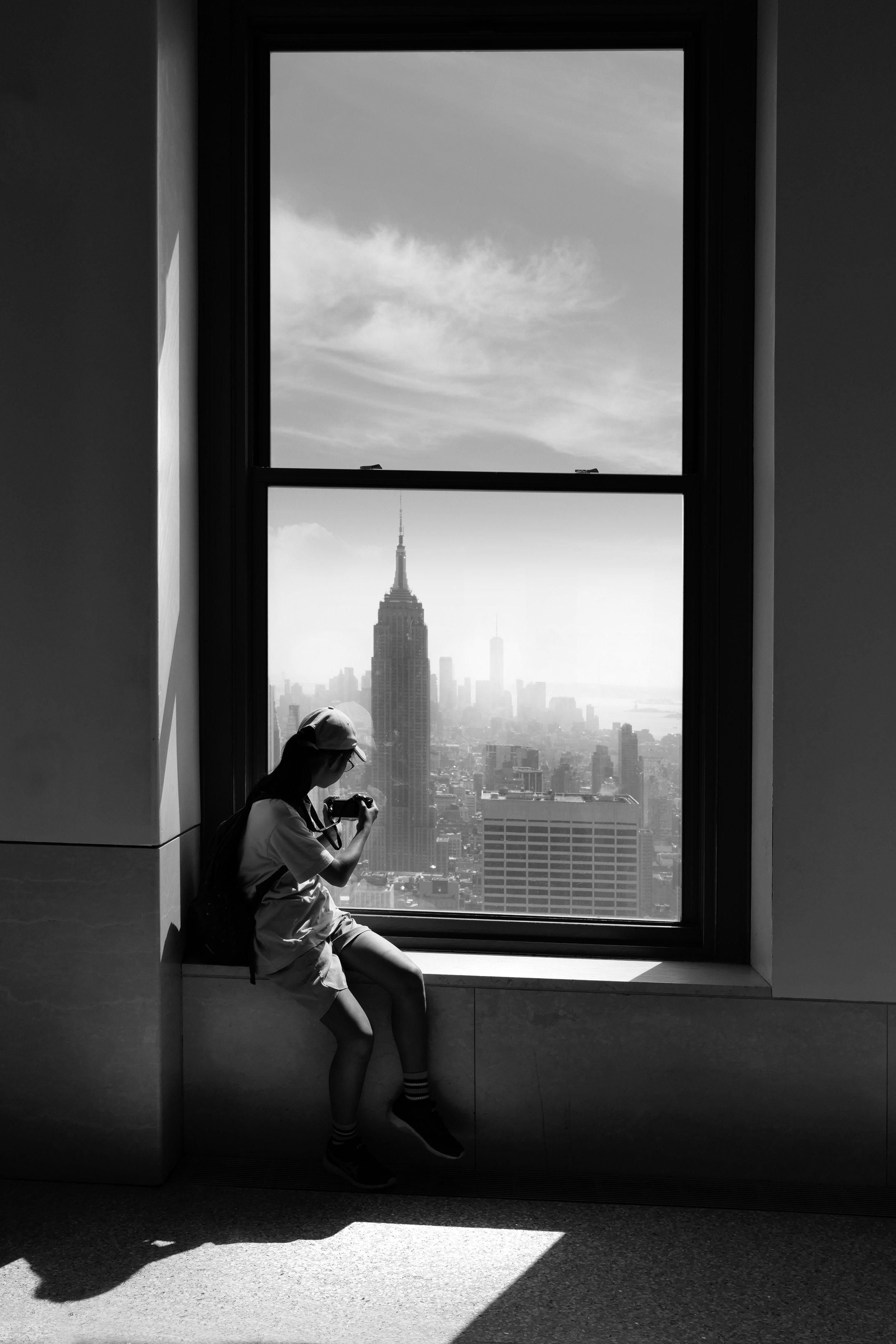 A person sitting by a window, taking a photo of New York City skyline including the Empire State Building.