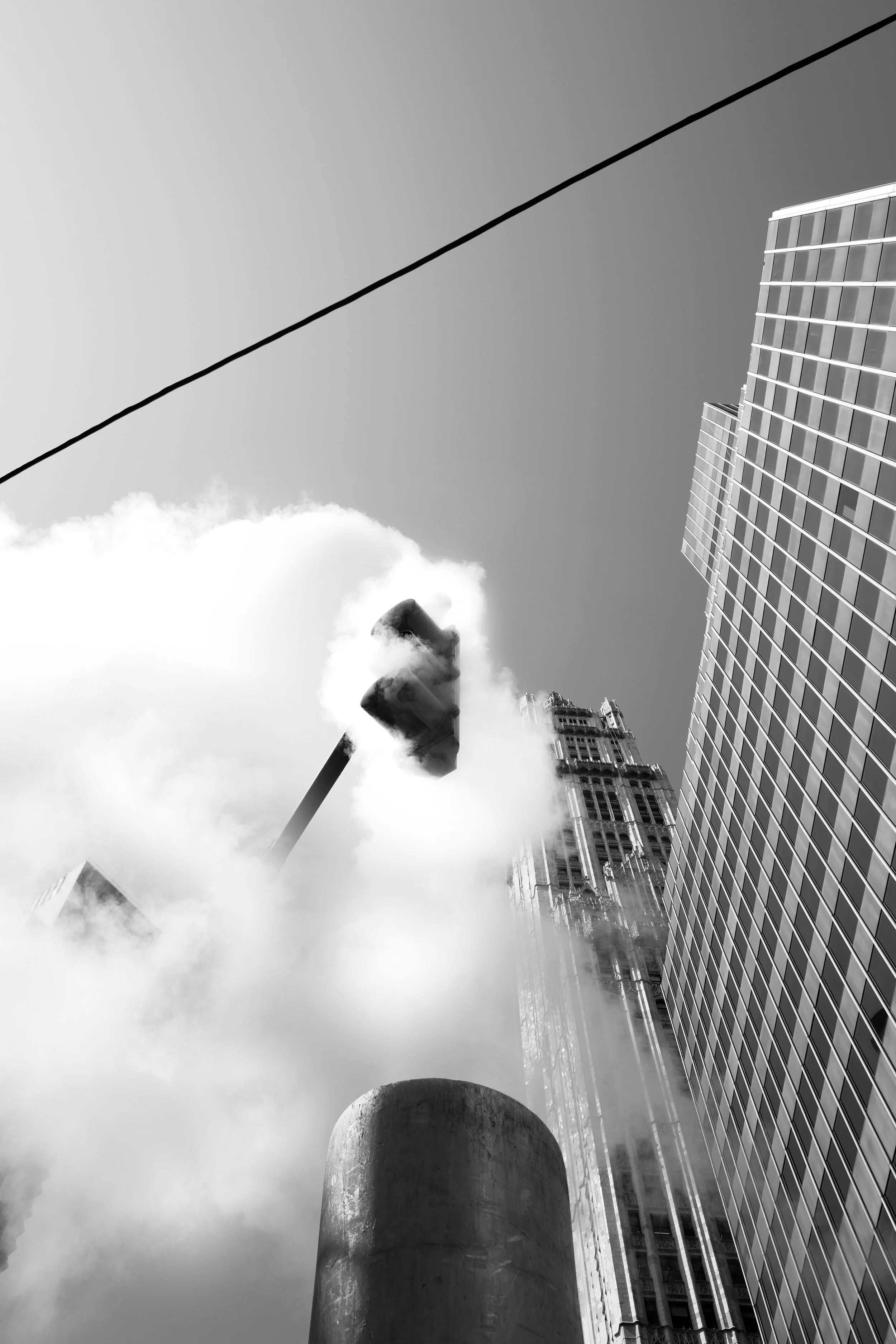 Black and white upward view of modern skyscrapers with clouds and smoke, city street scene.