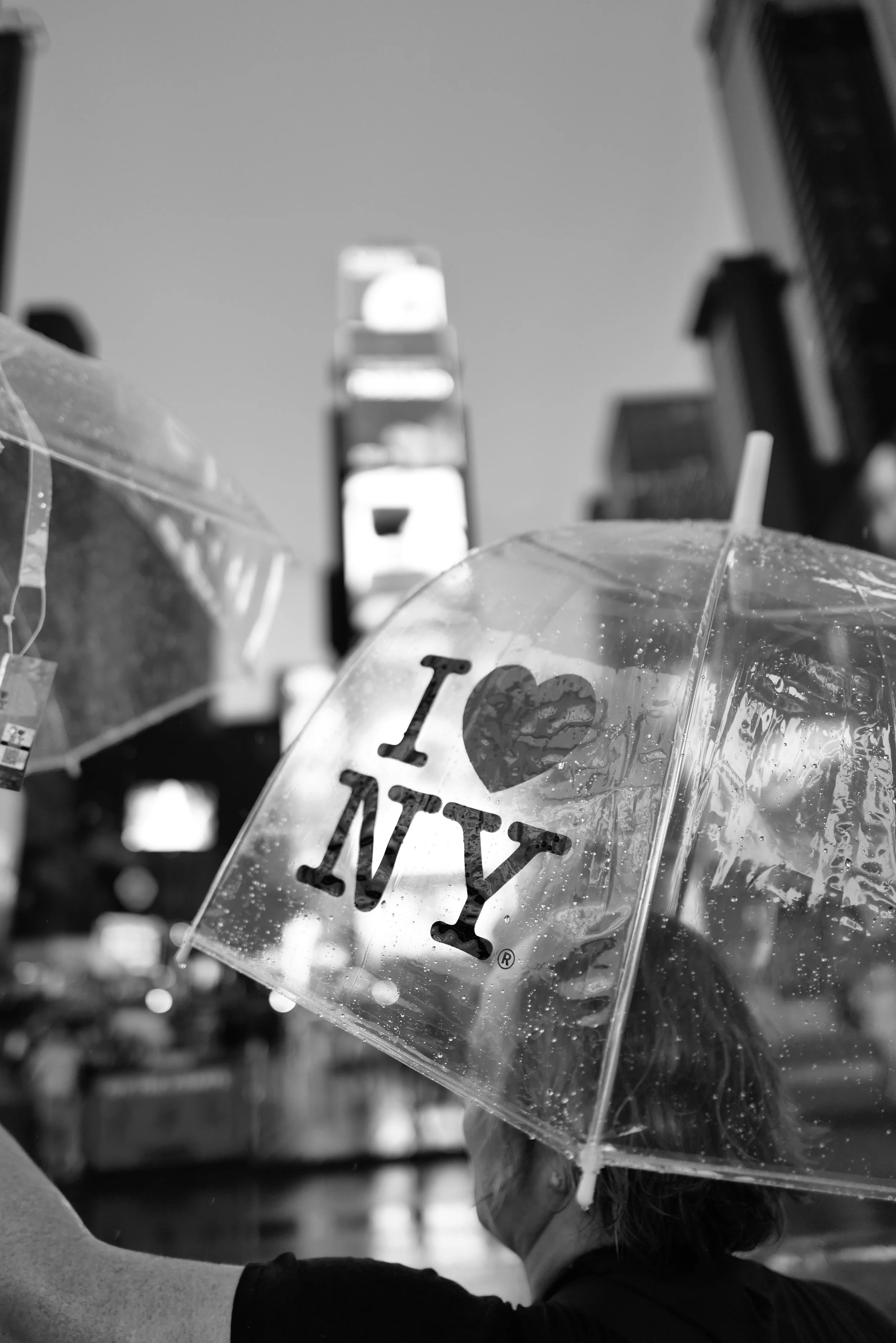 A person holding a transparent umbrella with the text "I love NY" on it, with part of their face and hair visible.
