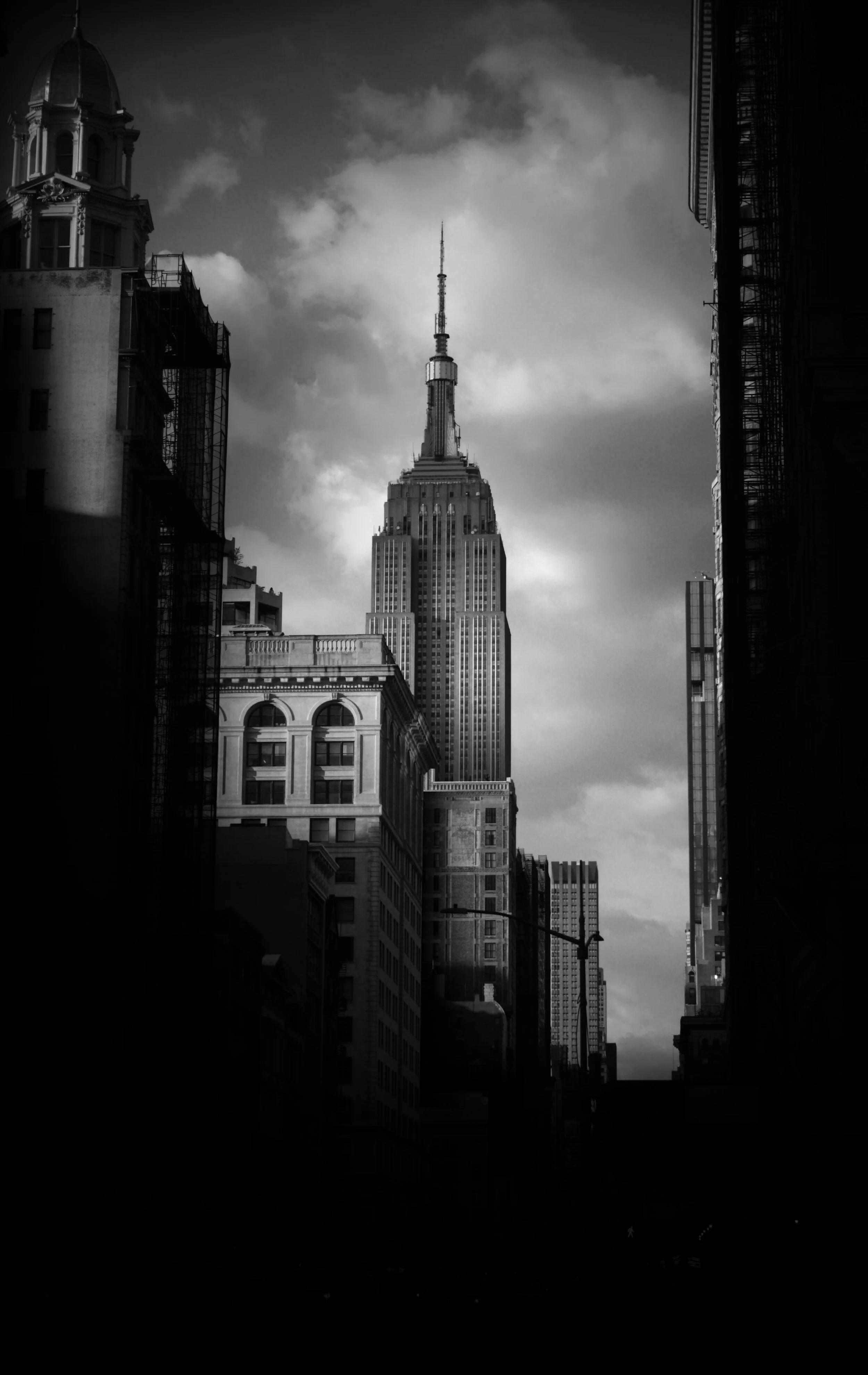 Black and white photo of the Empire State Building in New York City, surrounded by other tall buildings, with clouds in the sky.