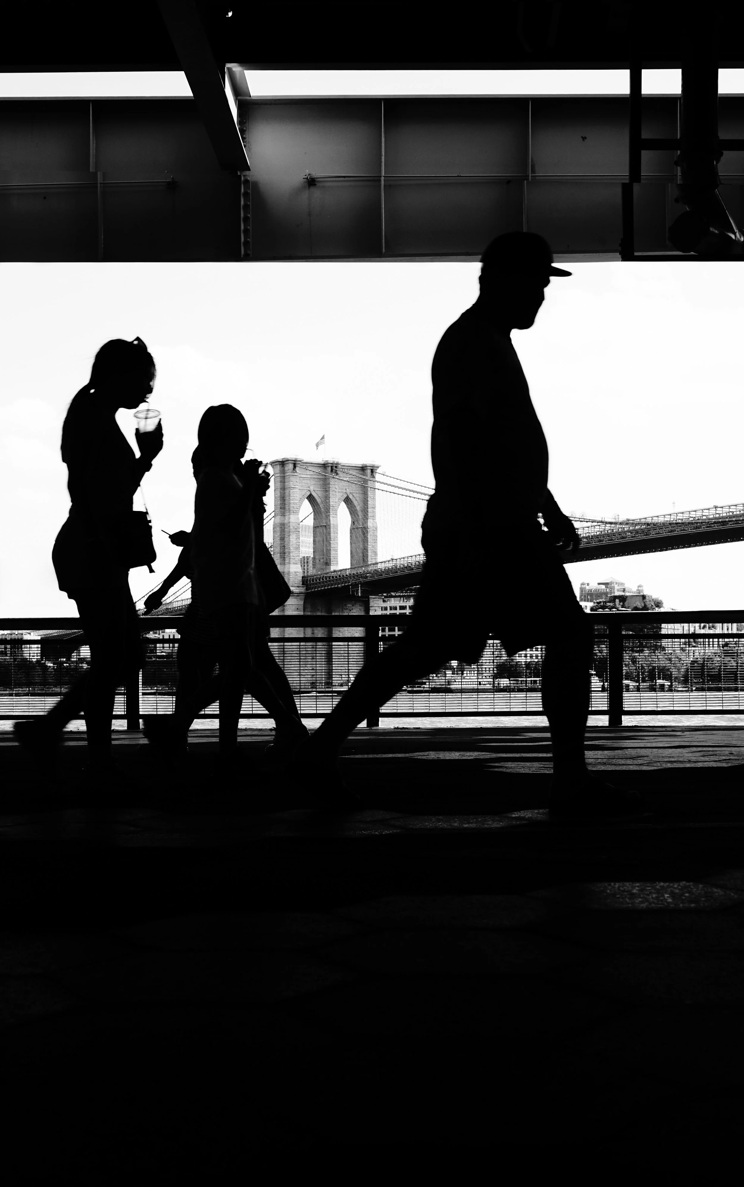 Silhouettes of four people walking under a bridge with the Brooklyn Bridge in the background.