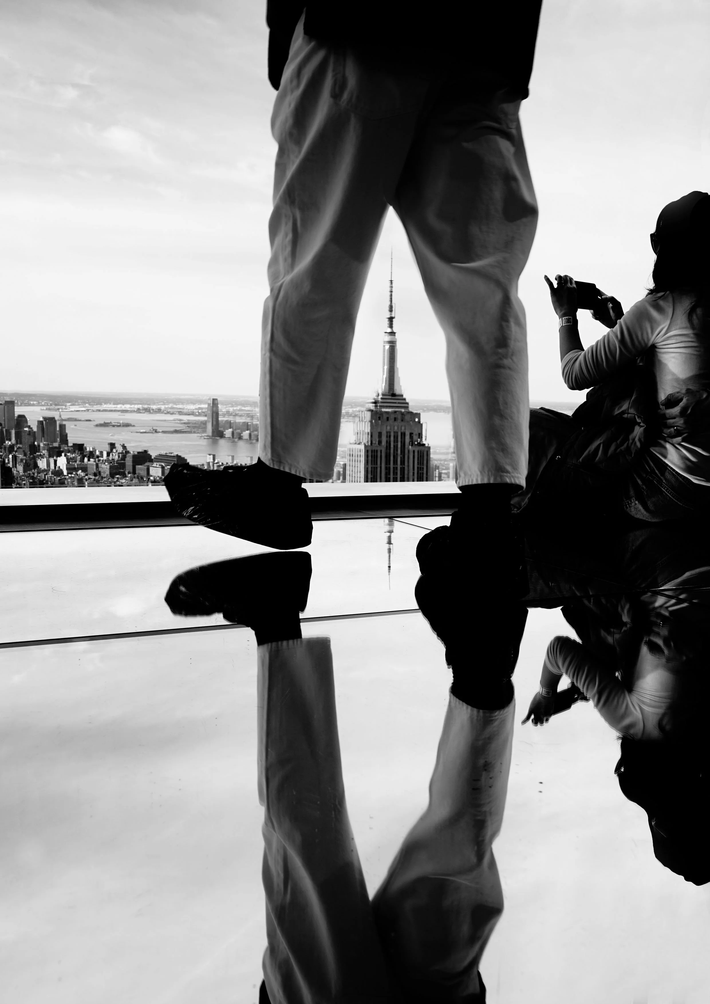 View from a high vantage point showing the Empire State Building in New York City with a reflection of people standing near a window.