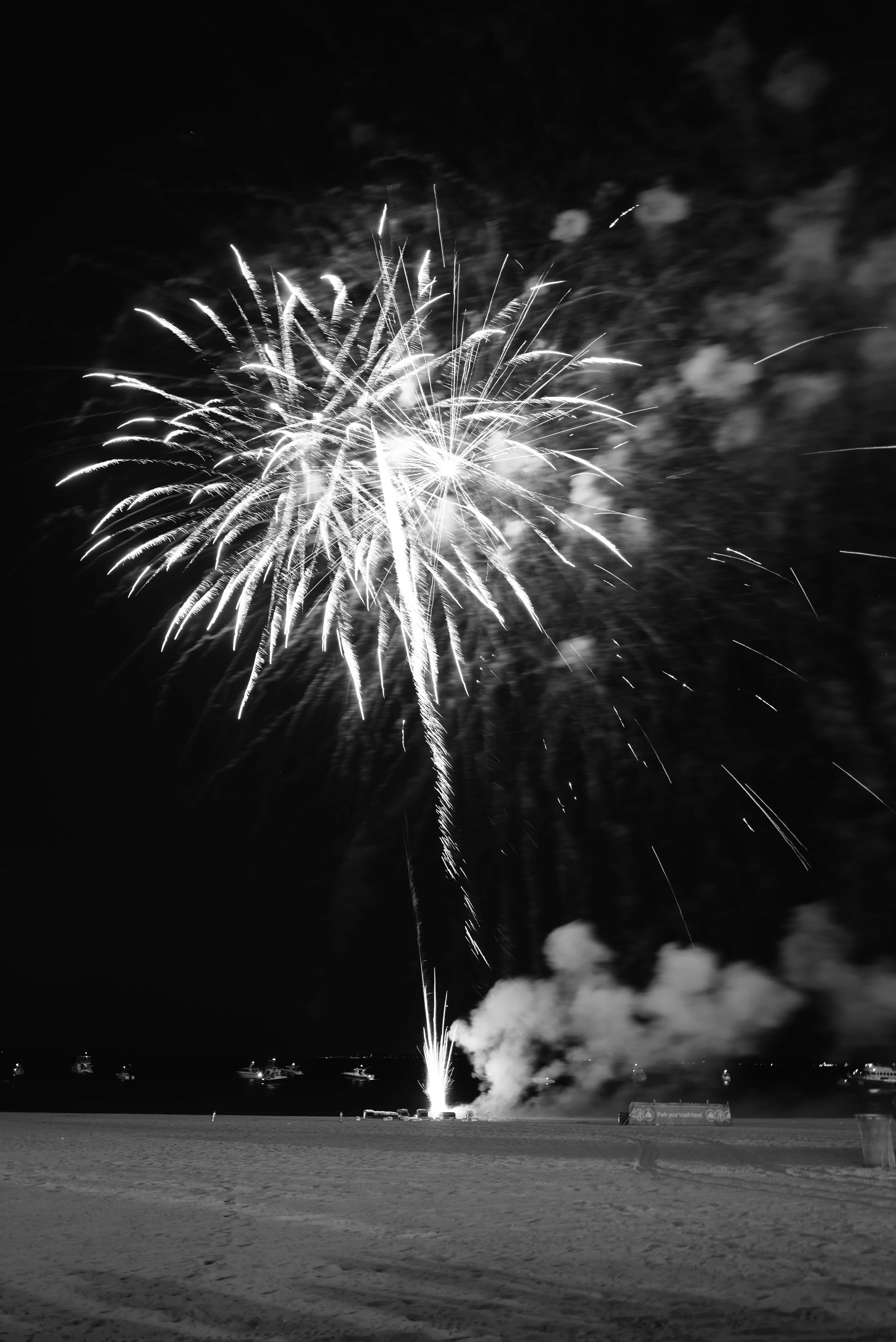 Fireworks exploding in the night sky over a beach with boats in the background.