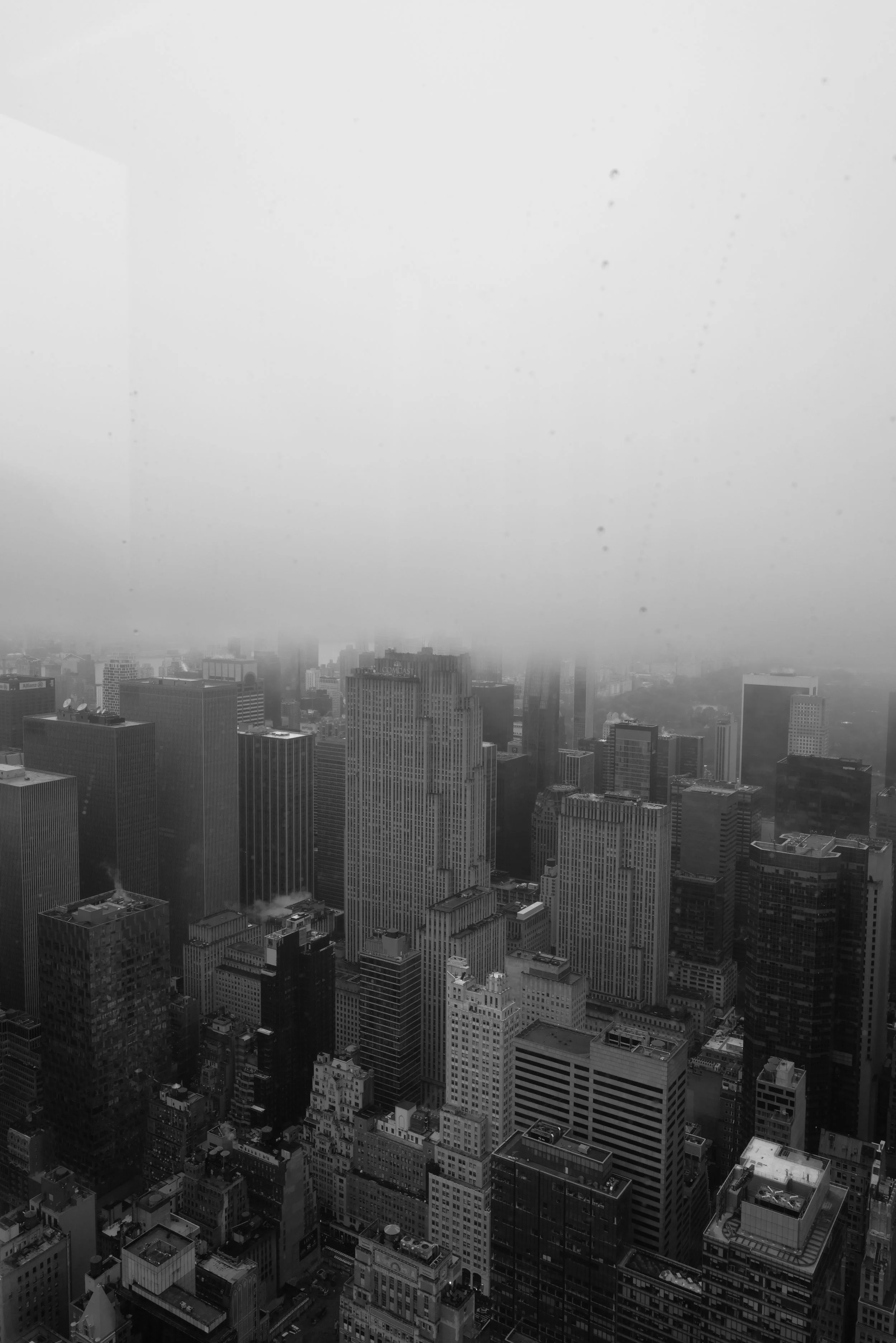 Black and white photo of a city skyline with tall skyscrapers on a foggy day, with thick fog obscuring the upper parts of the buildings.