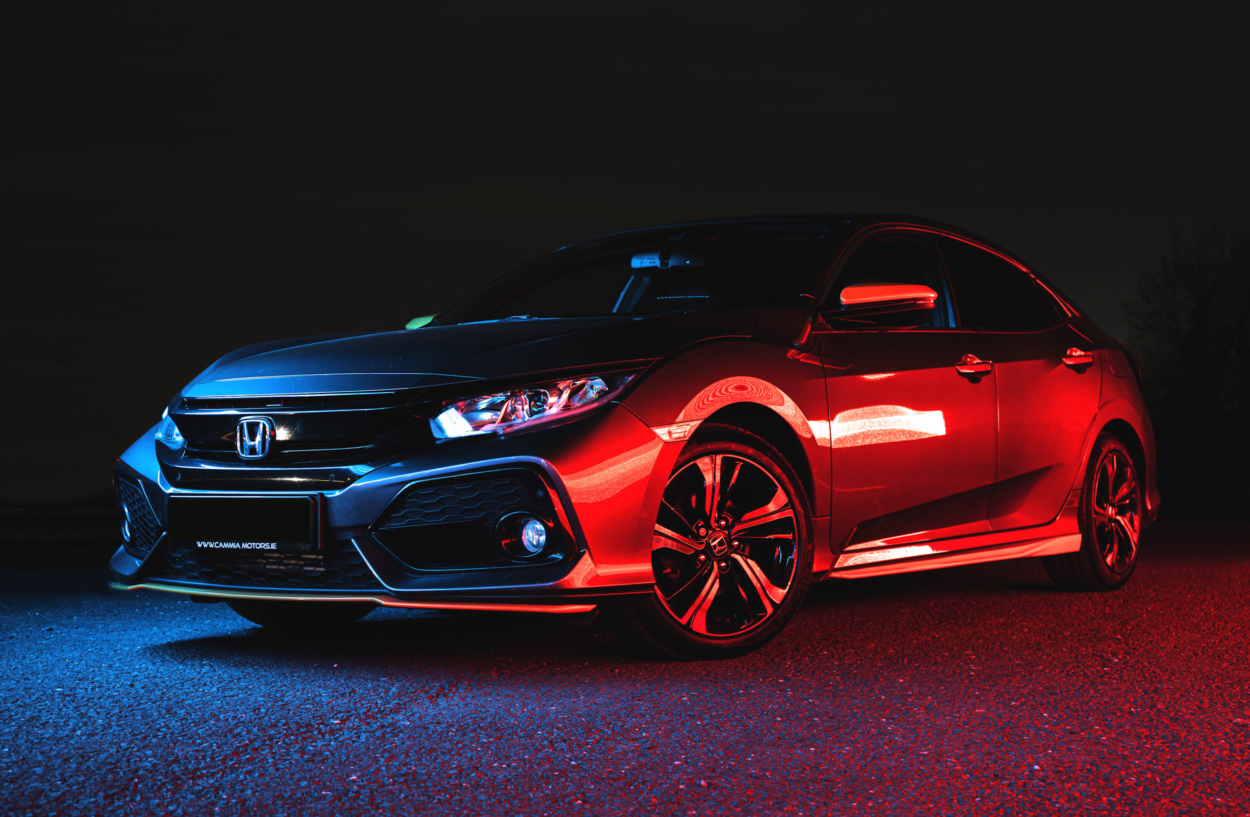 A black and red Honda sedan illuminated with blue and red lights at night.