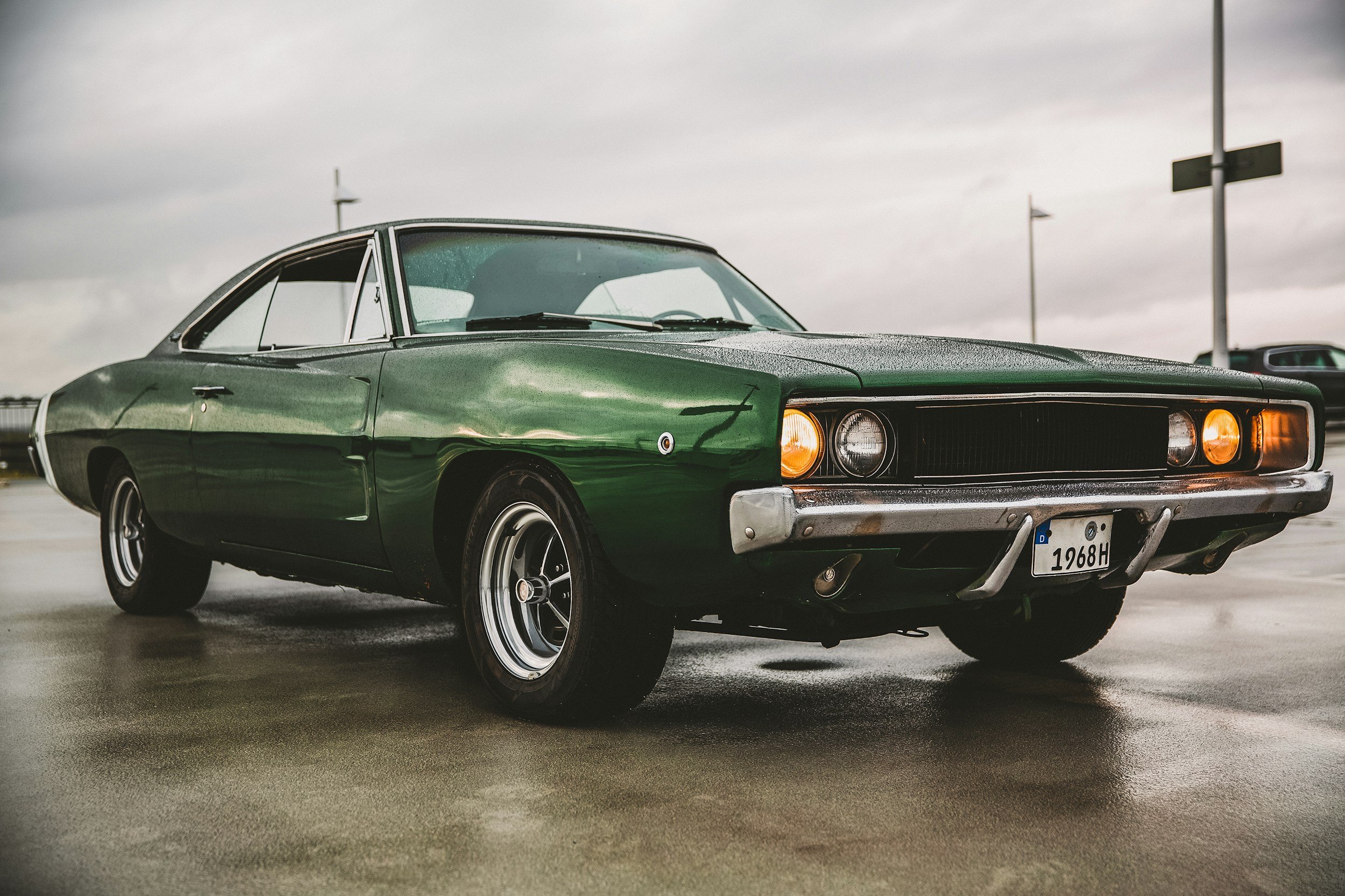 A classic green vintage car parked on an overcast day, with a wet surface reflecting the vehicle.