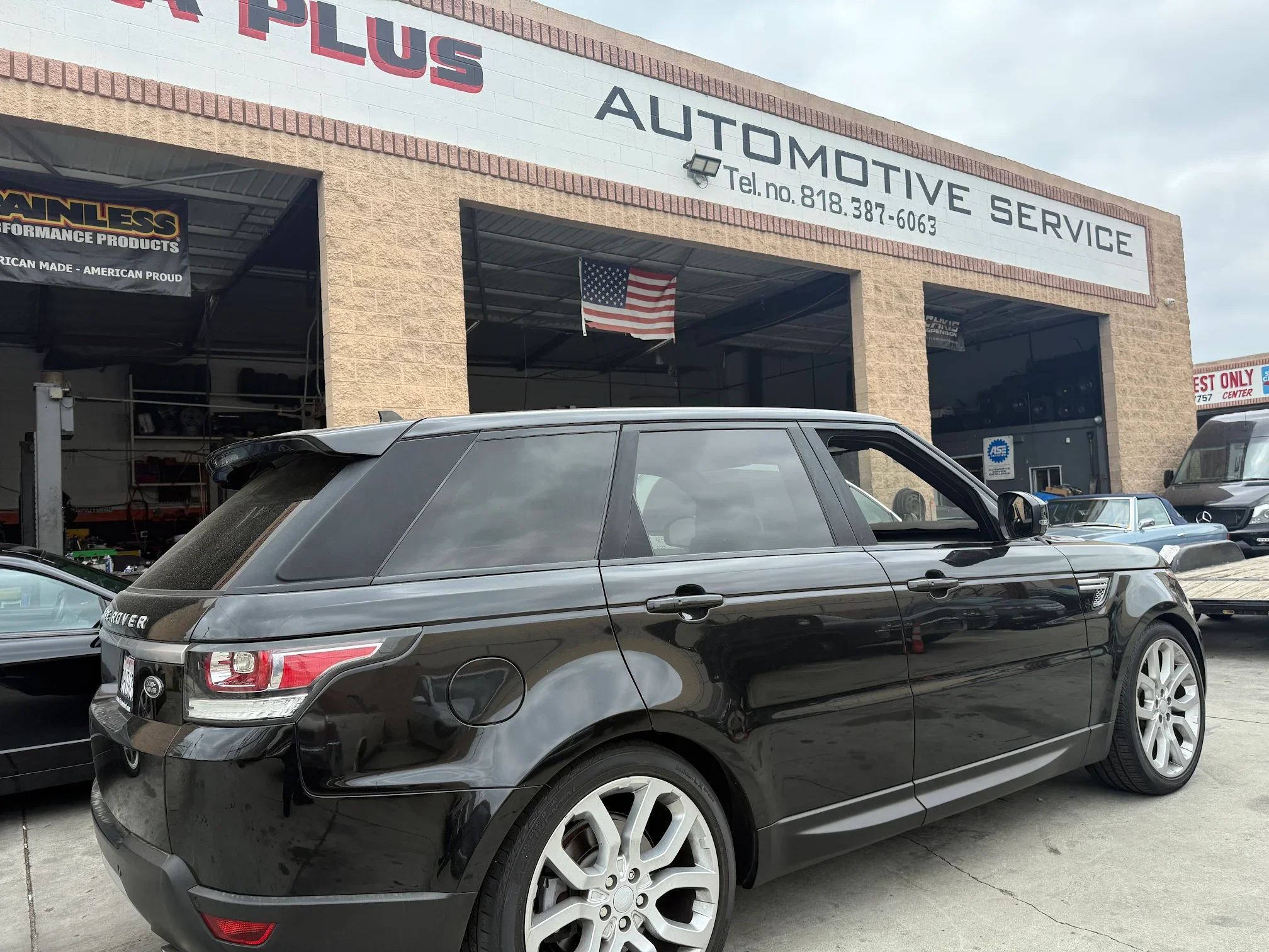 Black Range Rover parked in front of an automotive service shop with a sign reading 'Automotive Service' and American flag.