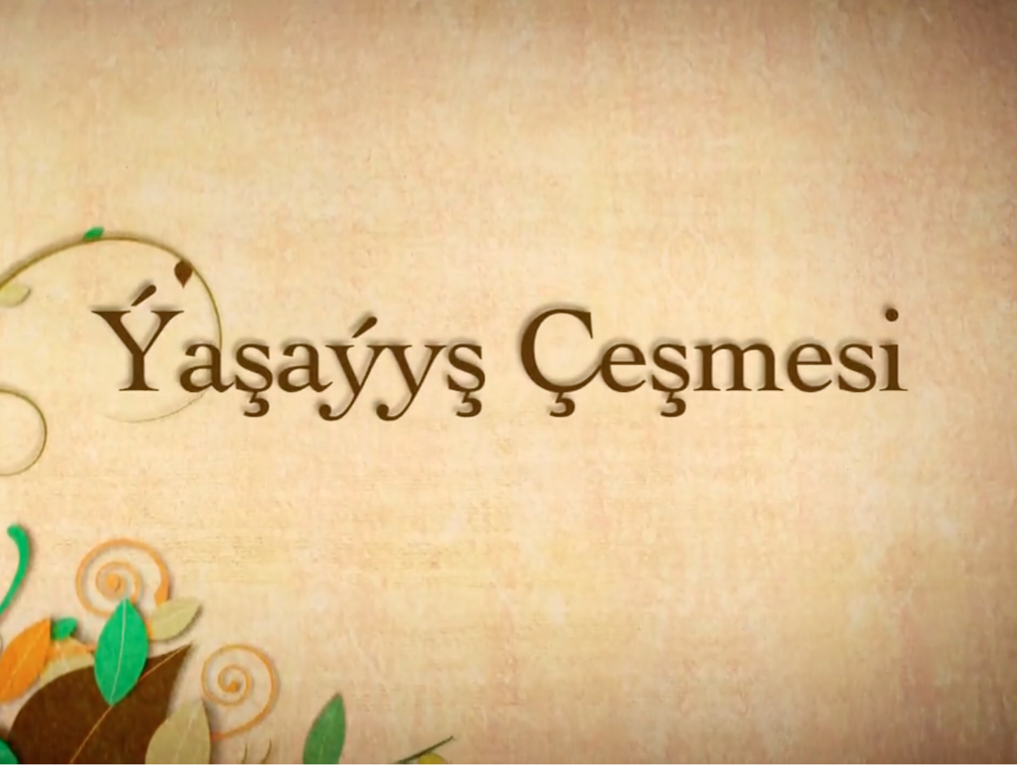 Bej reňkli dokumaly fonuň üstünde türkçe “Yaşayış Çeşmesi” jümlesi ýazylan, aşaky çep burçunda bezegli gülli nagyşlary bolan surat.