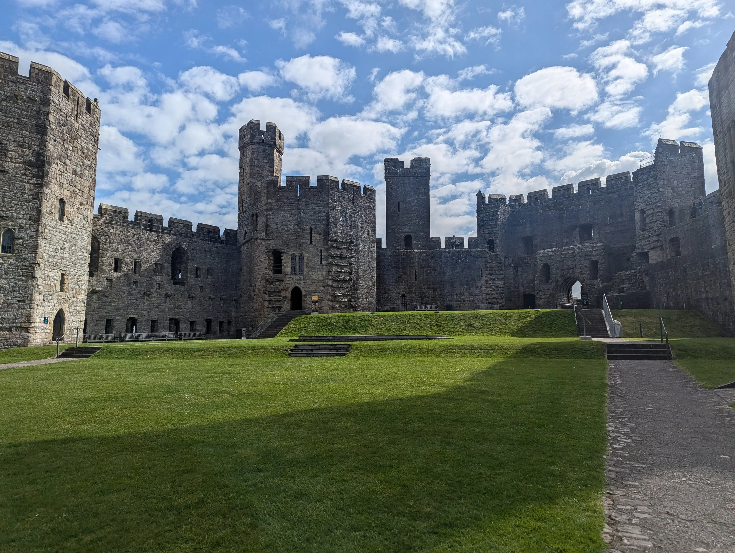 A scenic stone path leading through the historic inner courtyard of Caernarfon Castle in Wales, representing a custom land journey curated by Sunrise Travel destination specialists.