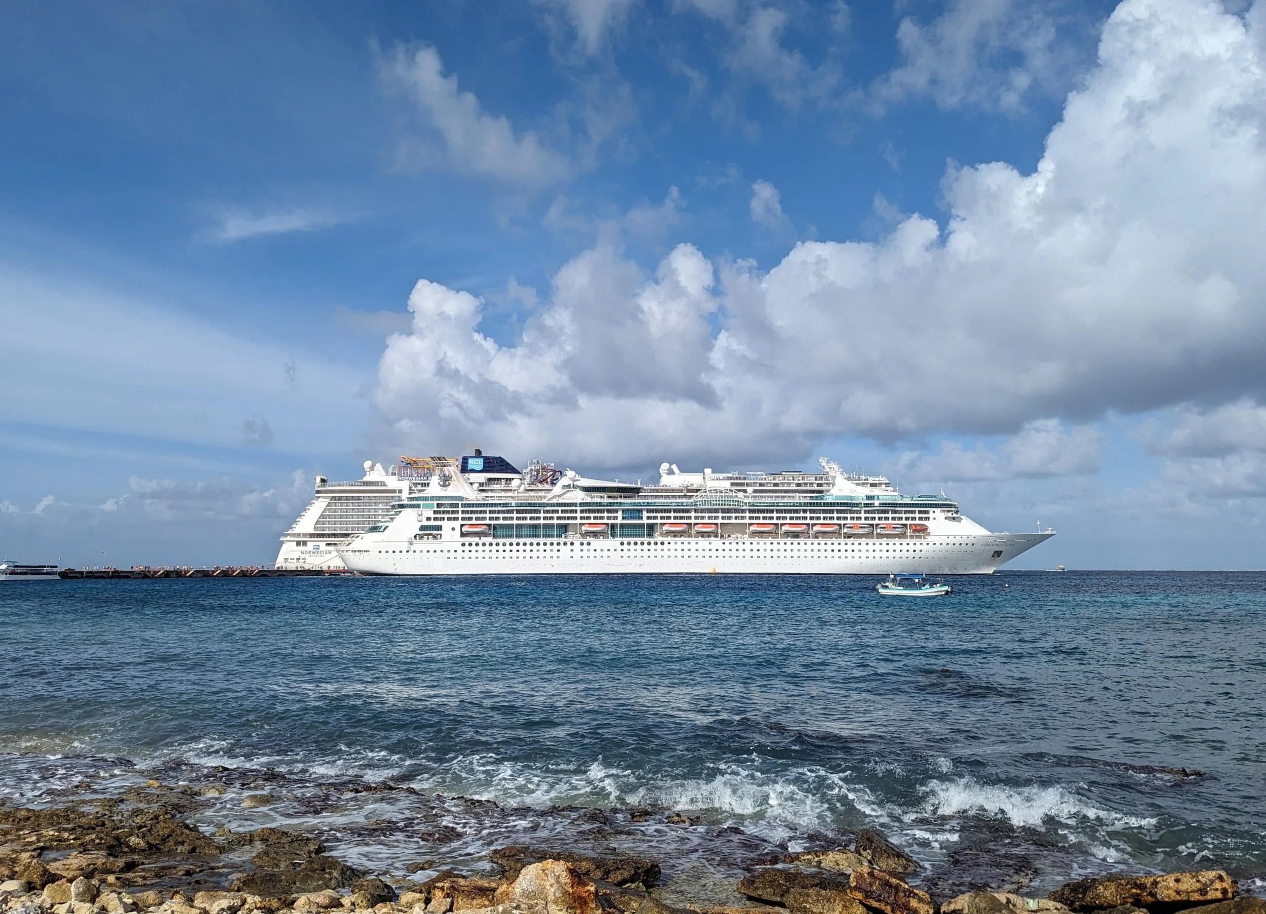 A Norwegian Cruise Line ship docked at a tropical shorline, representing the global ocean voyage expertise of Sunrise Travel, from the Caribbean to the Mediterranean.