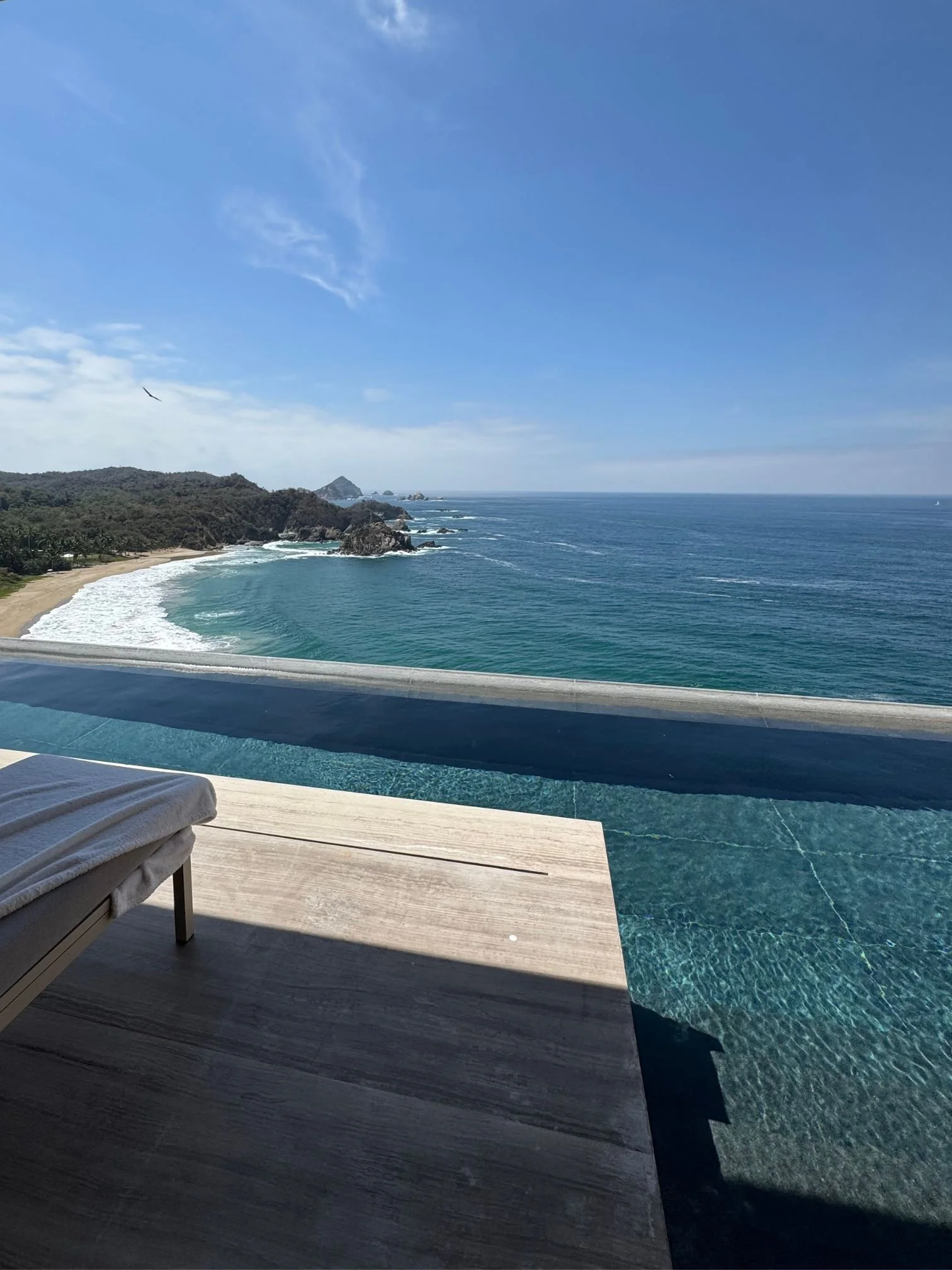 Luxury private infinity pool overlooking a tropical coastline and ocean at a Four Seasons resort, representing bespoke custom land vacation packages by Sunrise Travel.