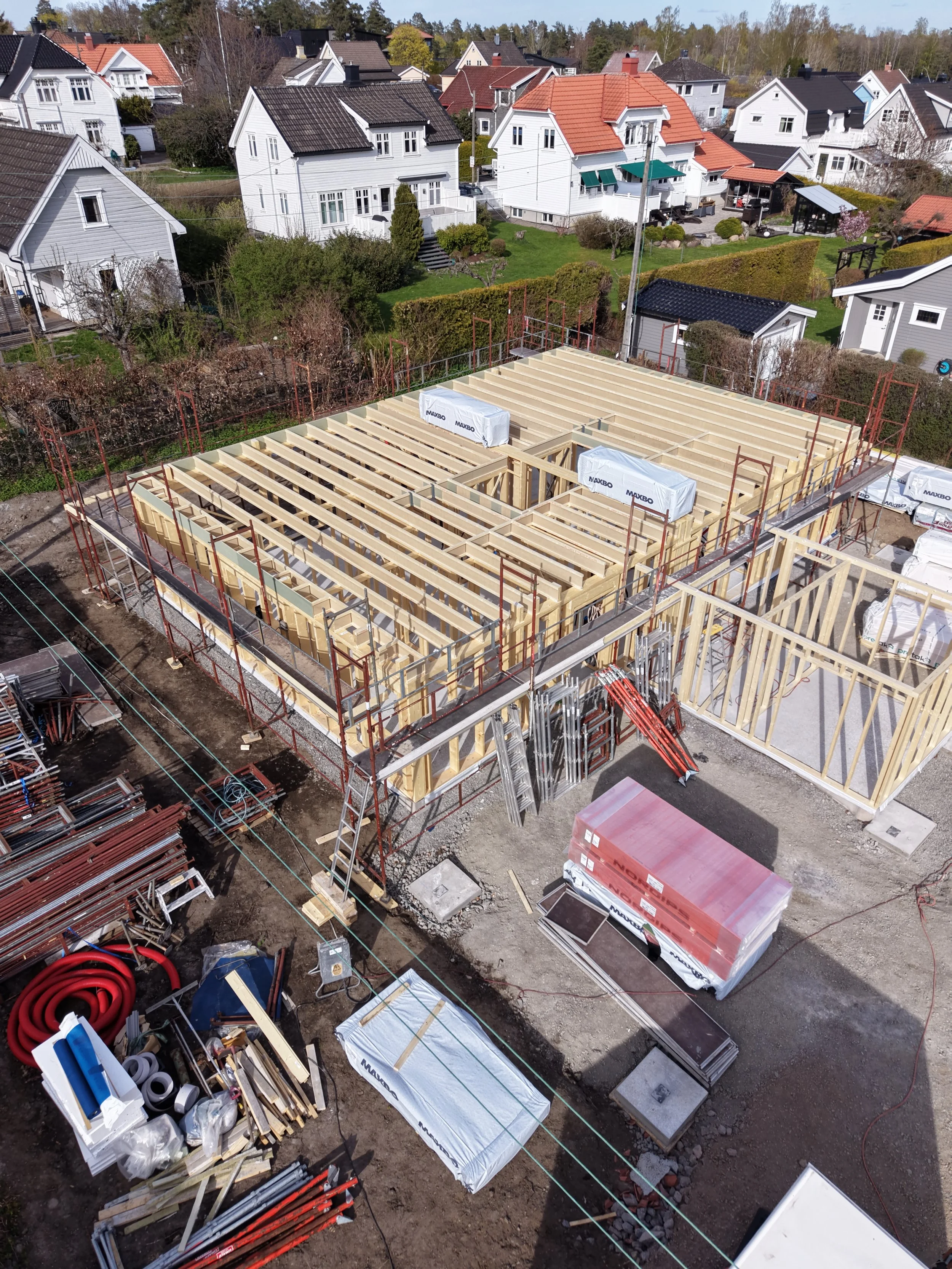 Trehus under oppførelse, sett ovenfra, med byggemateriell og verktøy rundt om på byggeplassen i en underutviklet fase. Reisverk. dronefoto