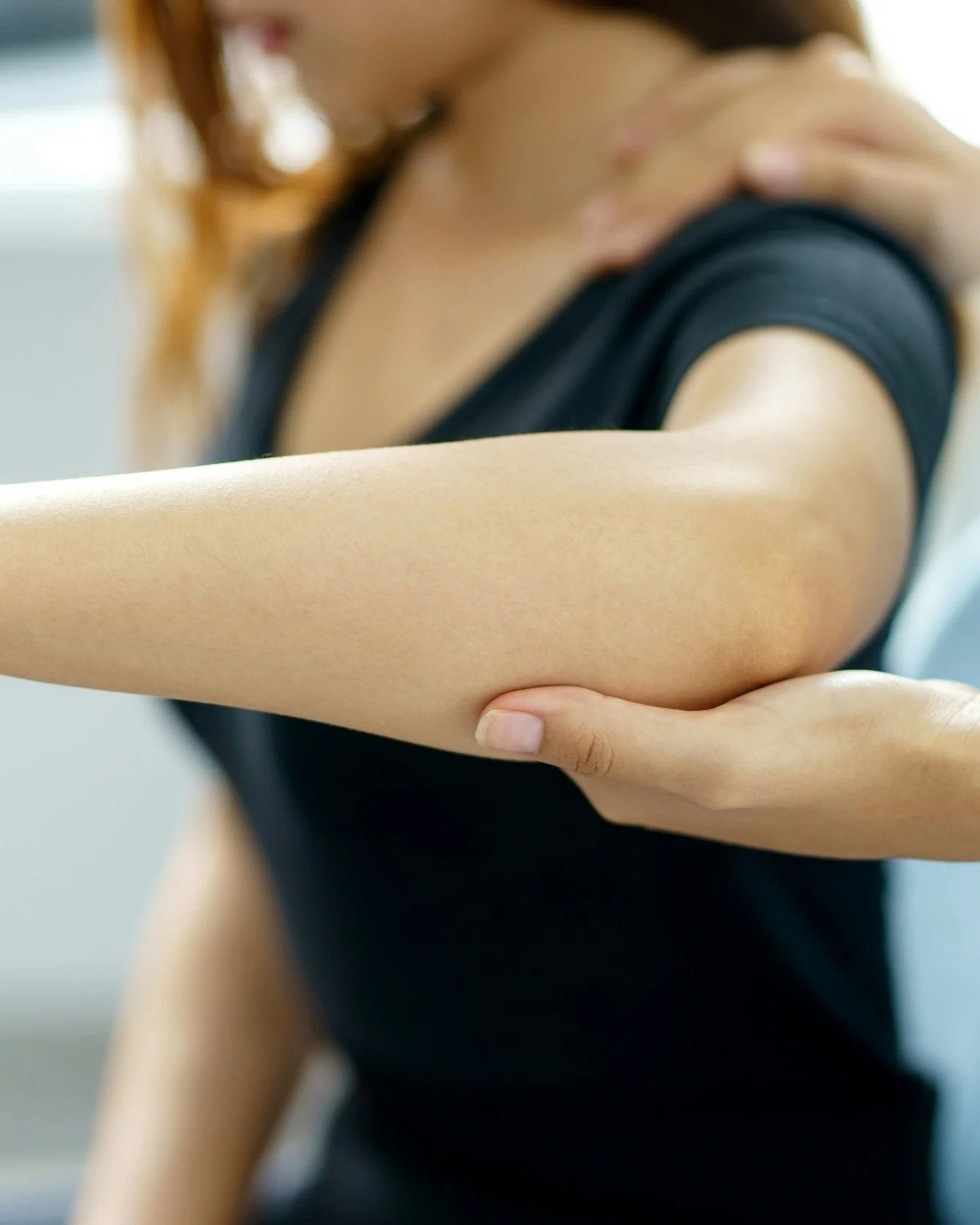 A person is holding their left arm with their right hand, showing the outer part of the arm and shoulder.