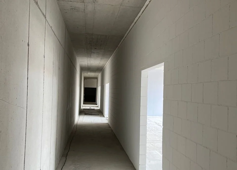 Leere, ungebaute Flur in einem Gebäude mit weißen Wänden und offenen Türen, Sicht zum Ende des Korridors