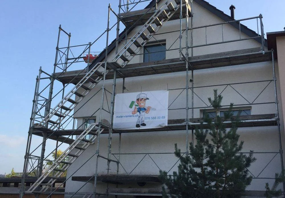 Ein Haus ist von Gerüsten umgeben, auf denen ein Banner mit einem Maler hängt. Das Haus hat mehrere Etagen, und es ist eine kleine Tanne im Vordergrund.