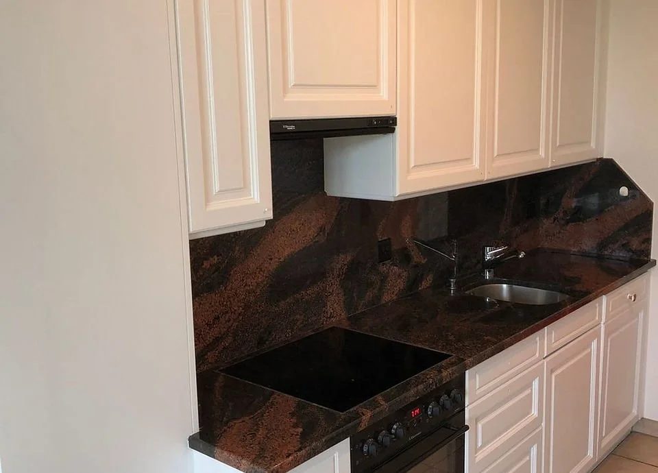 Küche mit weißen Schränken, dunklem Granit-Arbeitsplatte, Herd, Spüle und schwarzer Wandverkleidung.