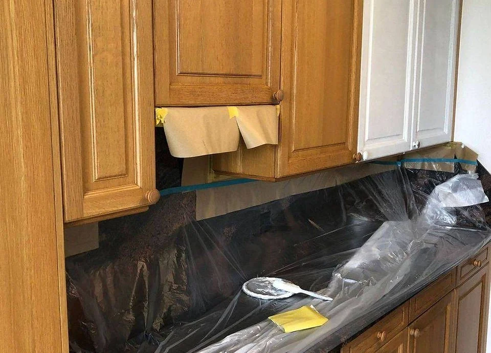 Küchenarbeitsplatte während Renovierungsarbeiten, mit schwarzer Abdeckfolie, Pinsel und Papier auf der Oberfläche