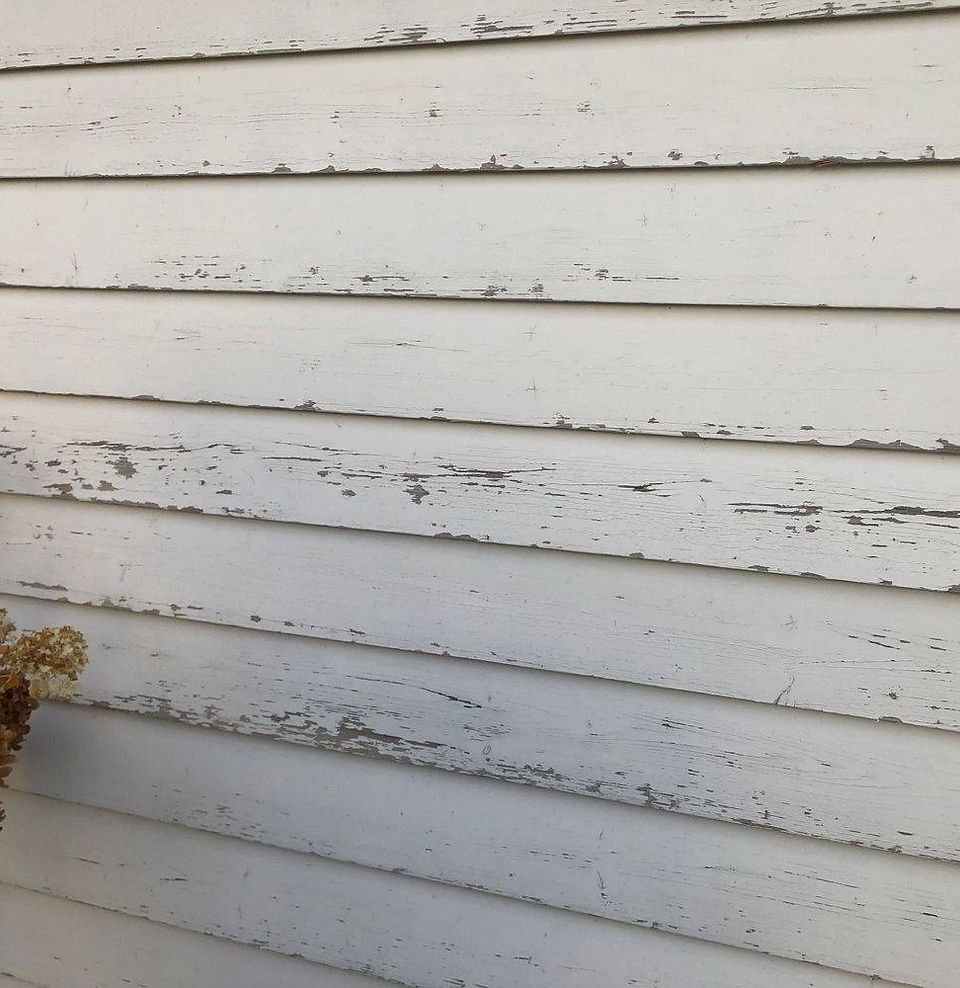 Verwitterte weiße Holzwand mit abgeblätterter Farbe.
