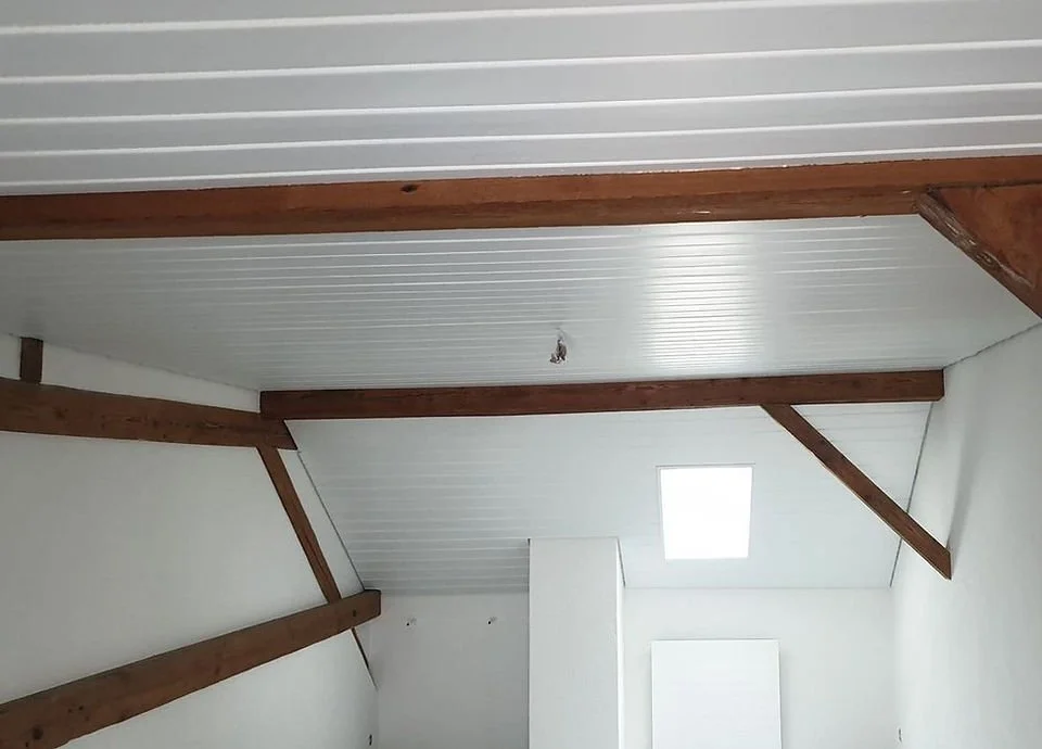 Innenansicht einer unmöblierten Dachgeschosswohnung mit weißen Wänden und Holzdeckenbalken.