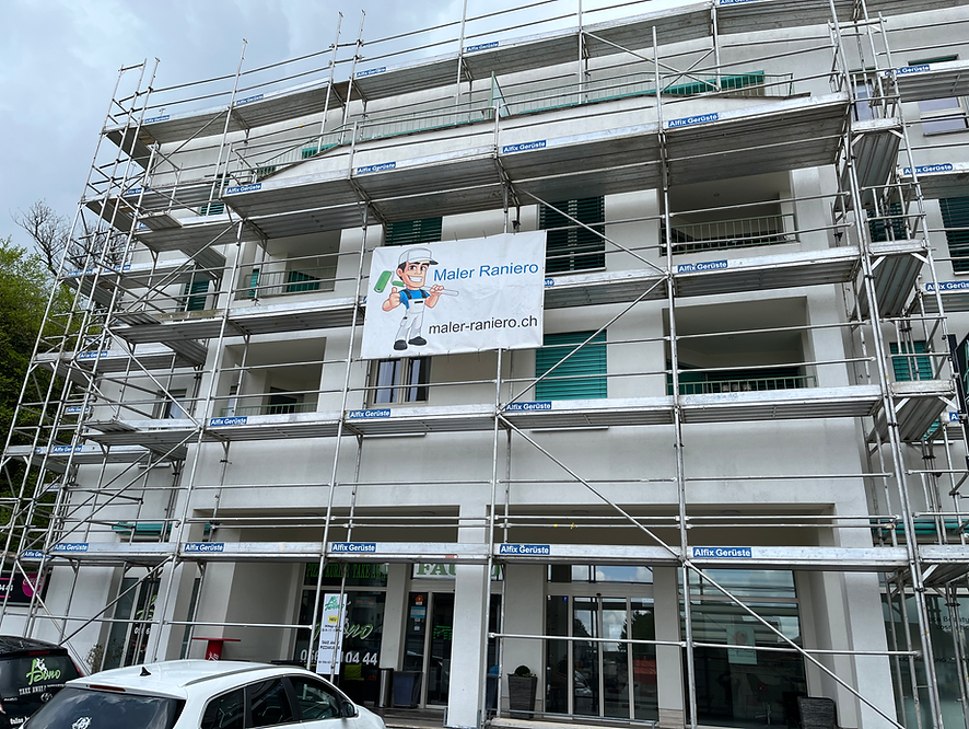 Baufassade eines Gebäudes mit Gerüsten und einem Schild eines Malers mit der Aufschrift "Maler Raniero" und der Website "maler-raniero.ch".
