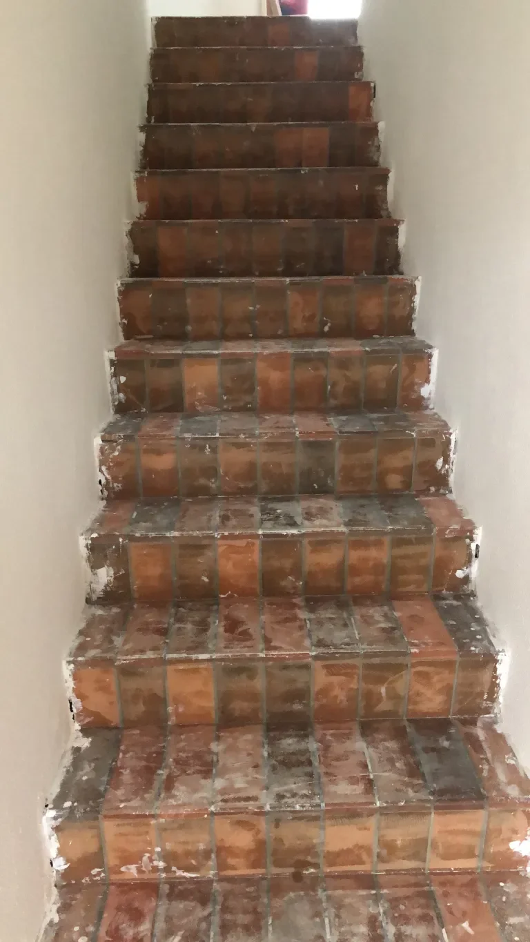Innenaufnahme einer Treppe mit unvollständiger Fliesenverlegung, teilweise noch ungespachtete Fugen, teilweise zuende verlegte rustikale Keramikfliesen in erdigen Farbtönen.