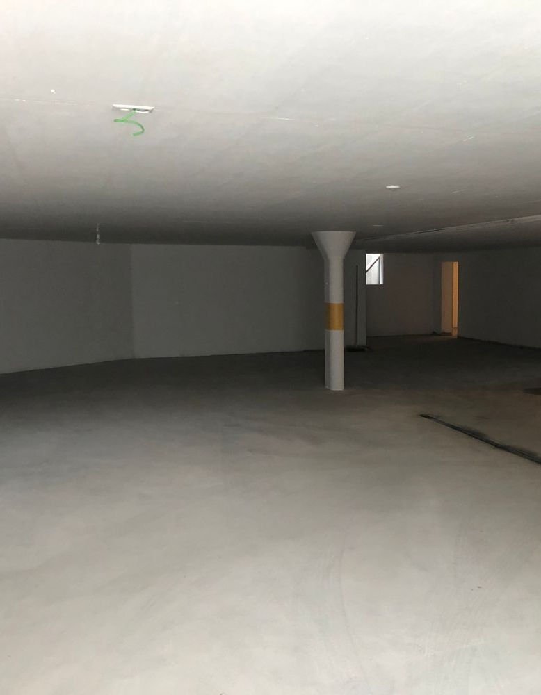 Leeres Parkhaus mit grauem Boden, weißen Wänden und wenigen Fenstern.