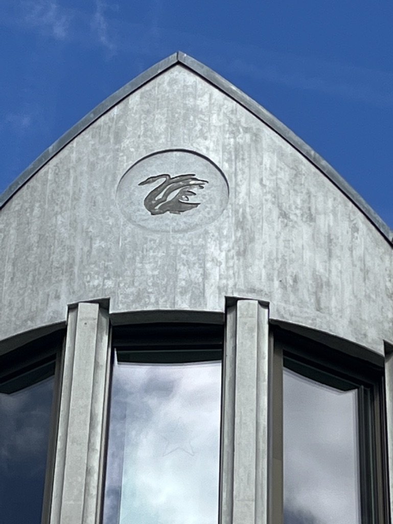 Fassade eines Gebäudes mit einem kreisförmigen Relief eines Vogels auf der oberen Wand, unter einem blauen Himmel.