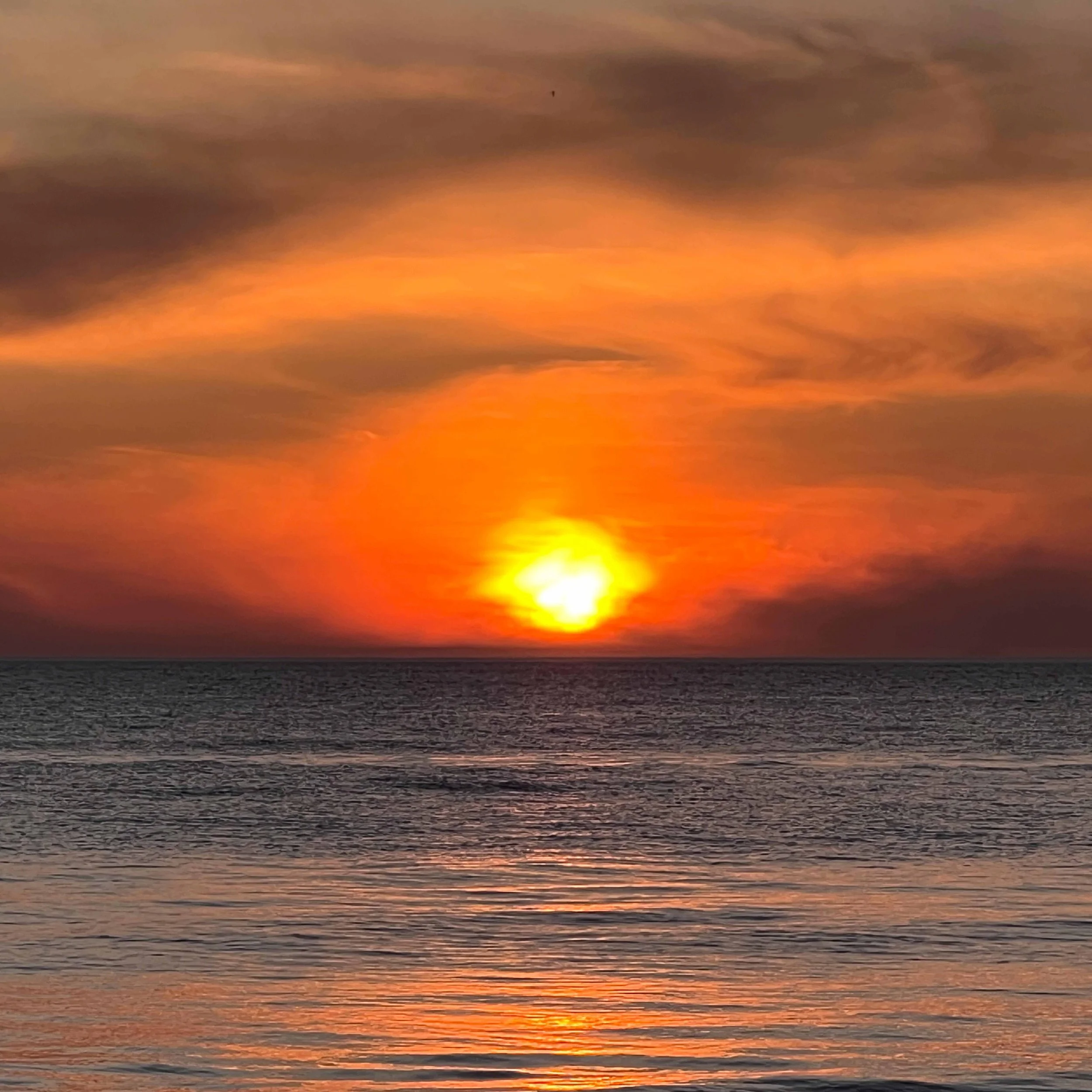 Sun setting over the ocean with colorful sky and clouds, orange and yellow hues reflecting on the water.