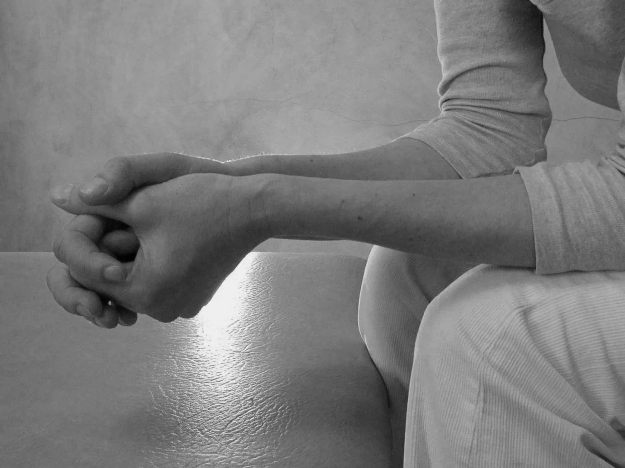 A person providing physical therapy or assistance by holding and supporting another person's arm and hand indoors.