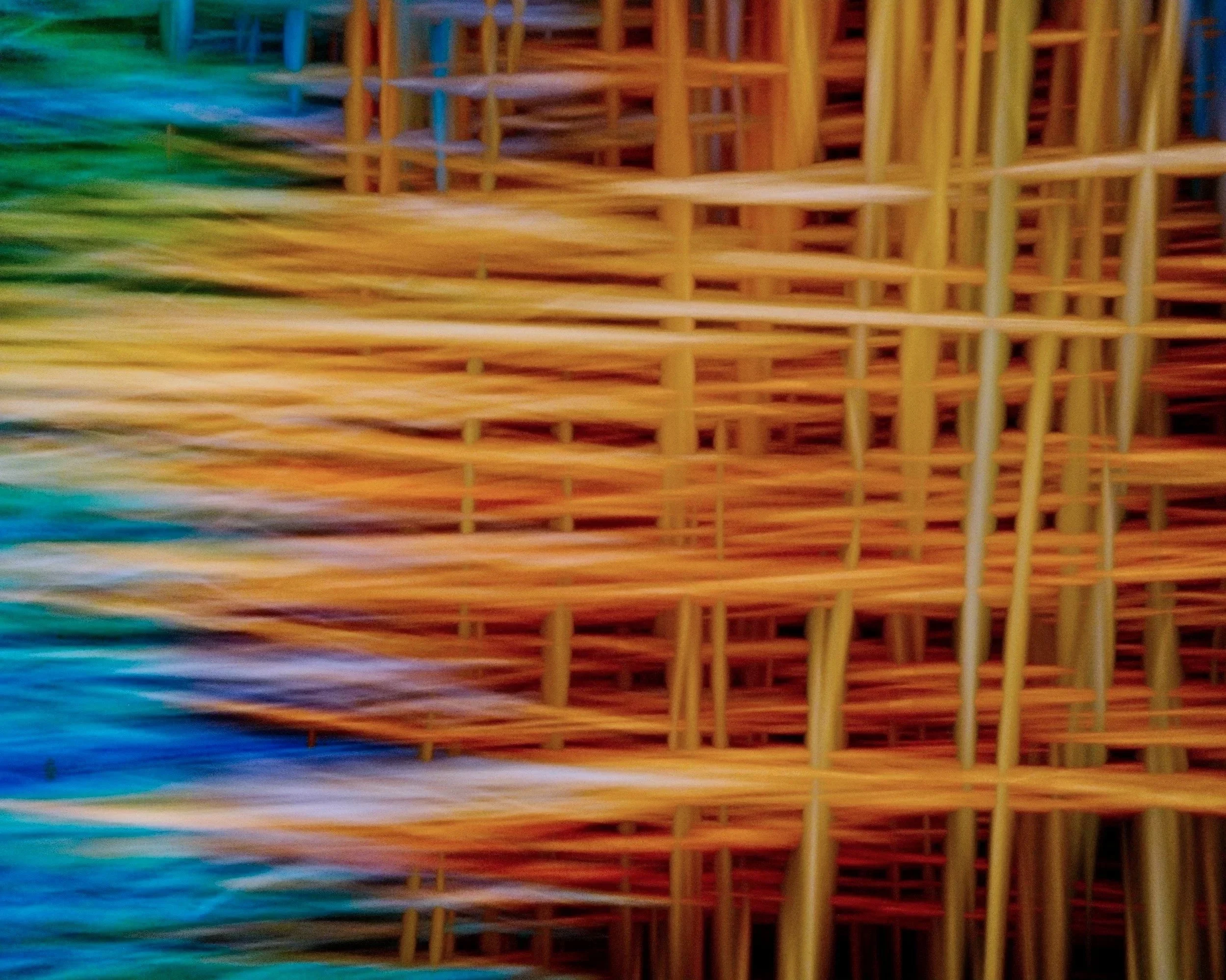 Close-up of woven straw or reed material in a gradient of vibrant colors including green, blue, orange, and yellow.