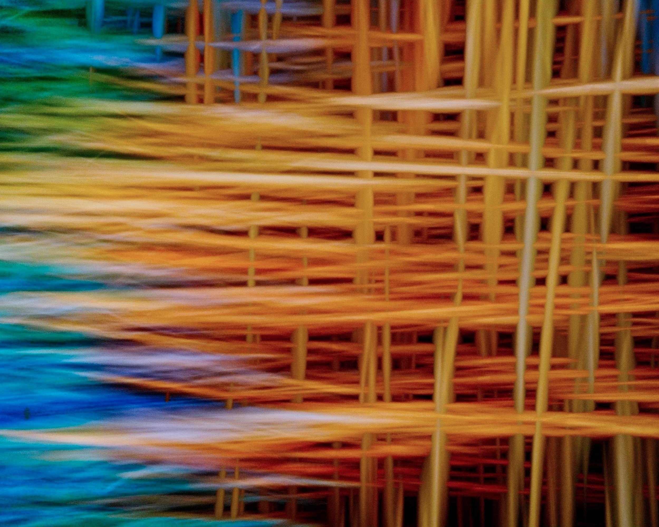 Close-up of woven straw or reed material in a gradient of vibrant colors including green, blue, orange, and yellow.