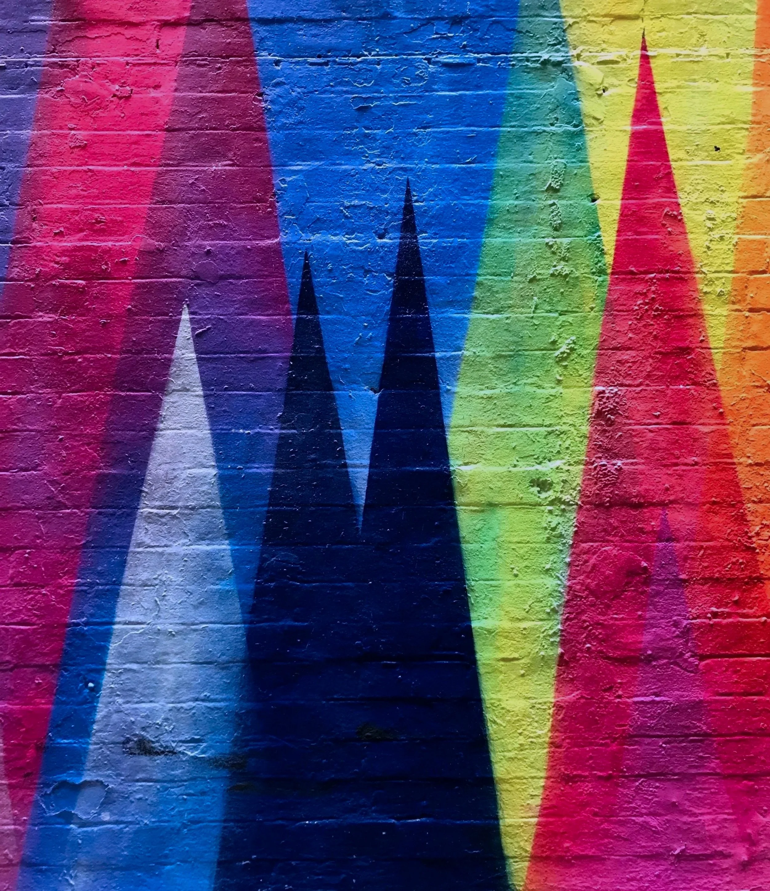 Colorful graffiti wall with rainbow-colored triangles and peaks.