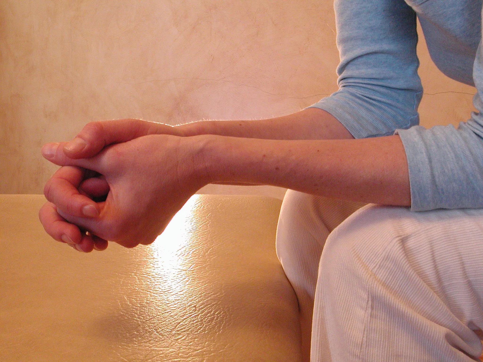 A person providing physical therapy or assistance by holding and supporting another person's arm and hand indoors.
