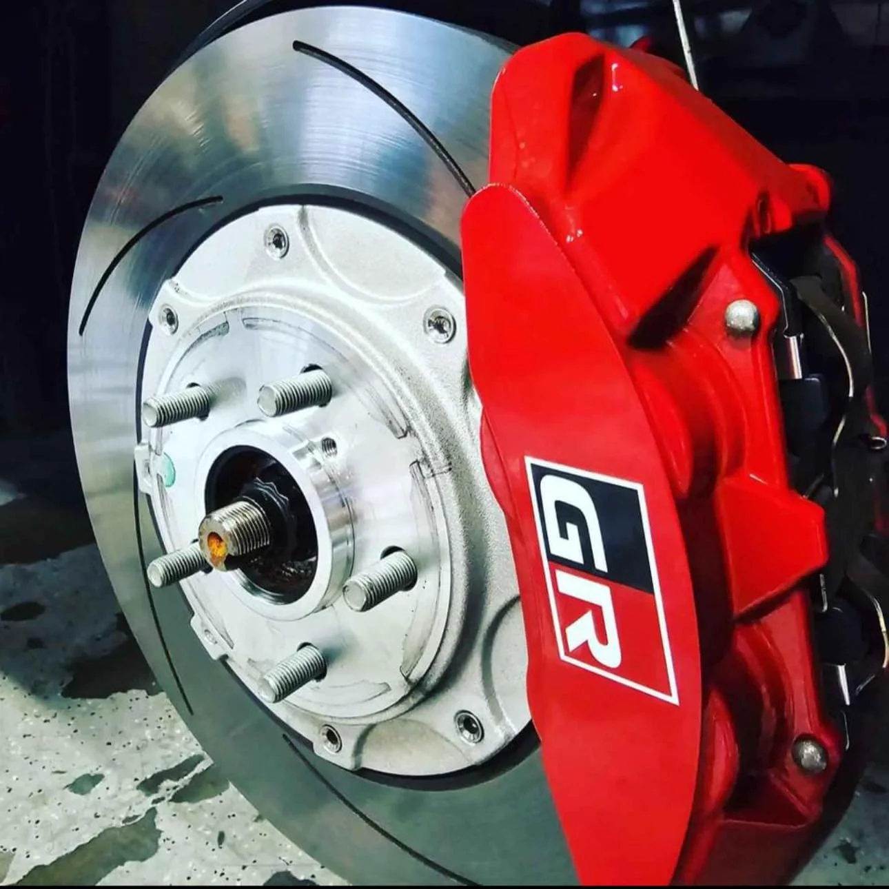 Close-up of a car brake rotor and caliper. The rotor is shiny metal with visible machining marks, and the red caliper has a GTR logo.