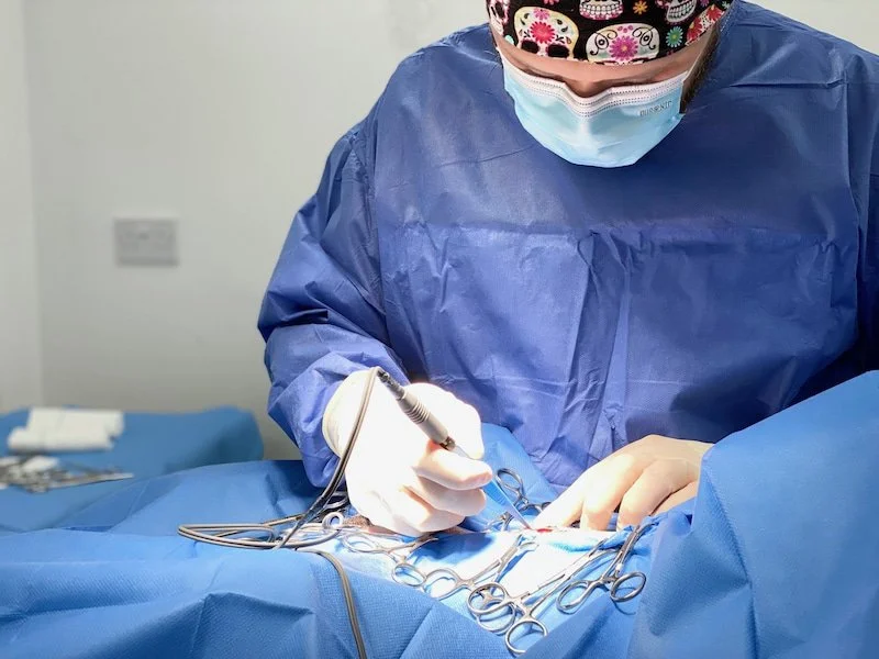 A surgeon dressed in blue scrubs, wearing a colorful face mask and white gloves, performing surgery in an operating room.