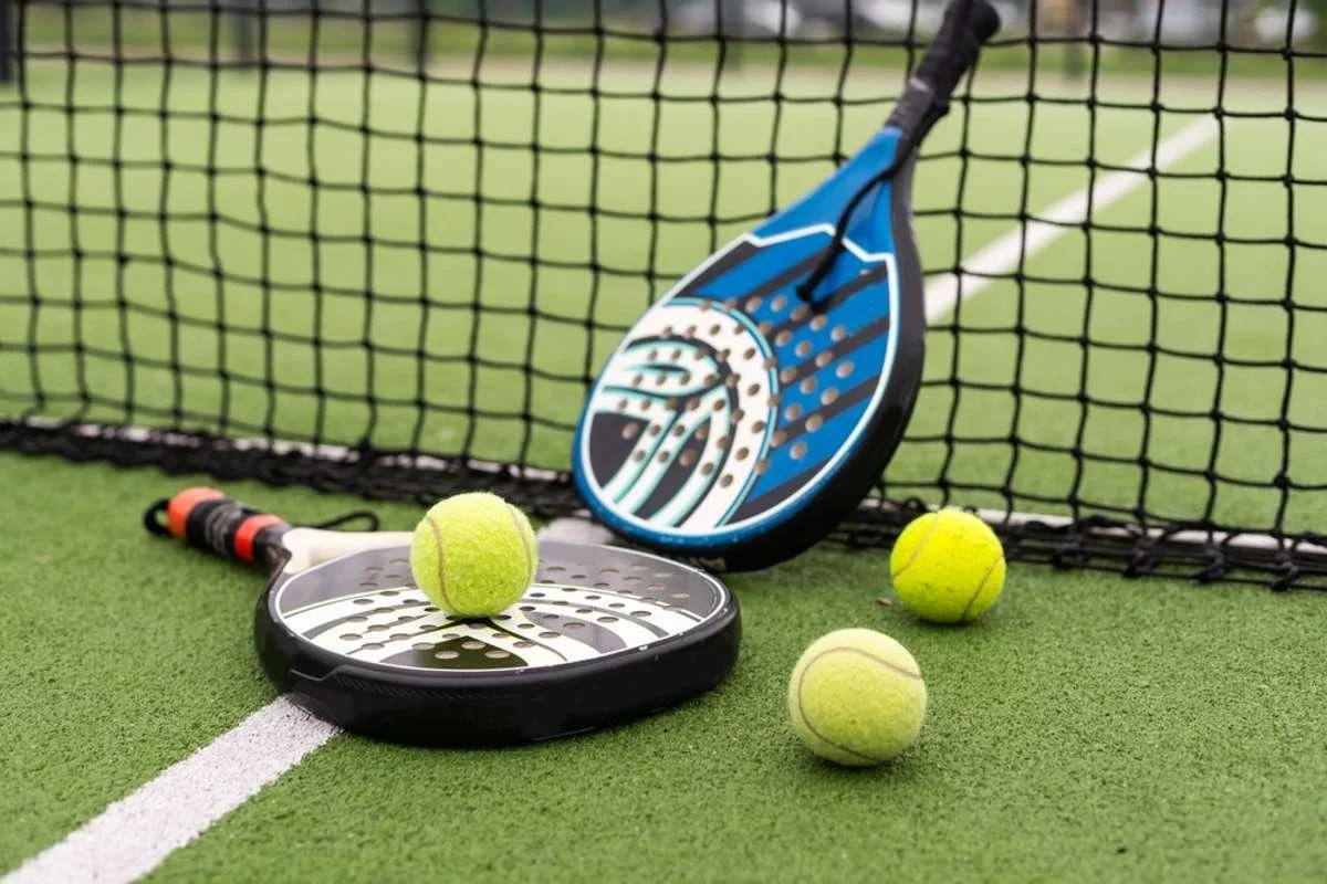 Tennis balls and paddles on an outdoor tennis court near the net.