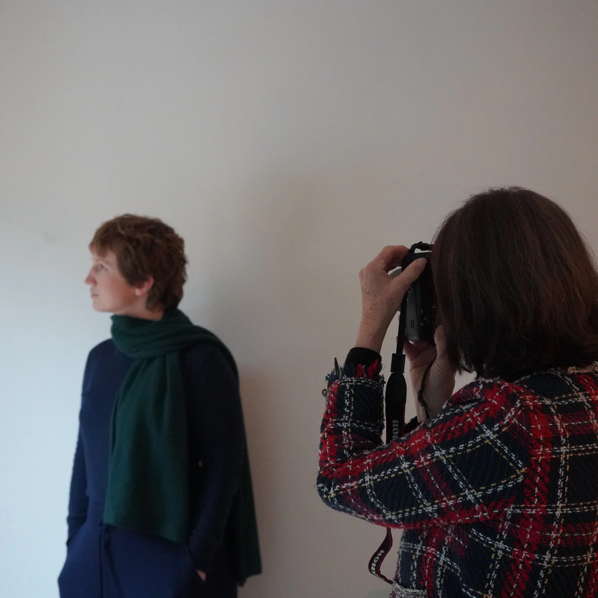 A lush green backyard with large trees and a small wooden table with two chairs. There is a small treehouse on a branch in one of the trees, and a swing hanging from another. The scene is sunlit, creating a peaceful outdoor setting.