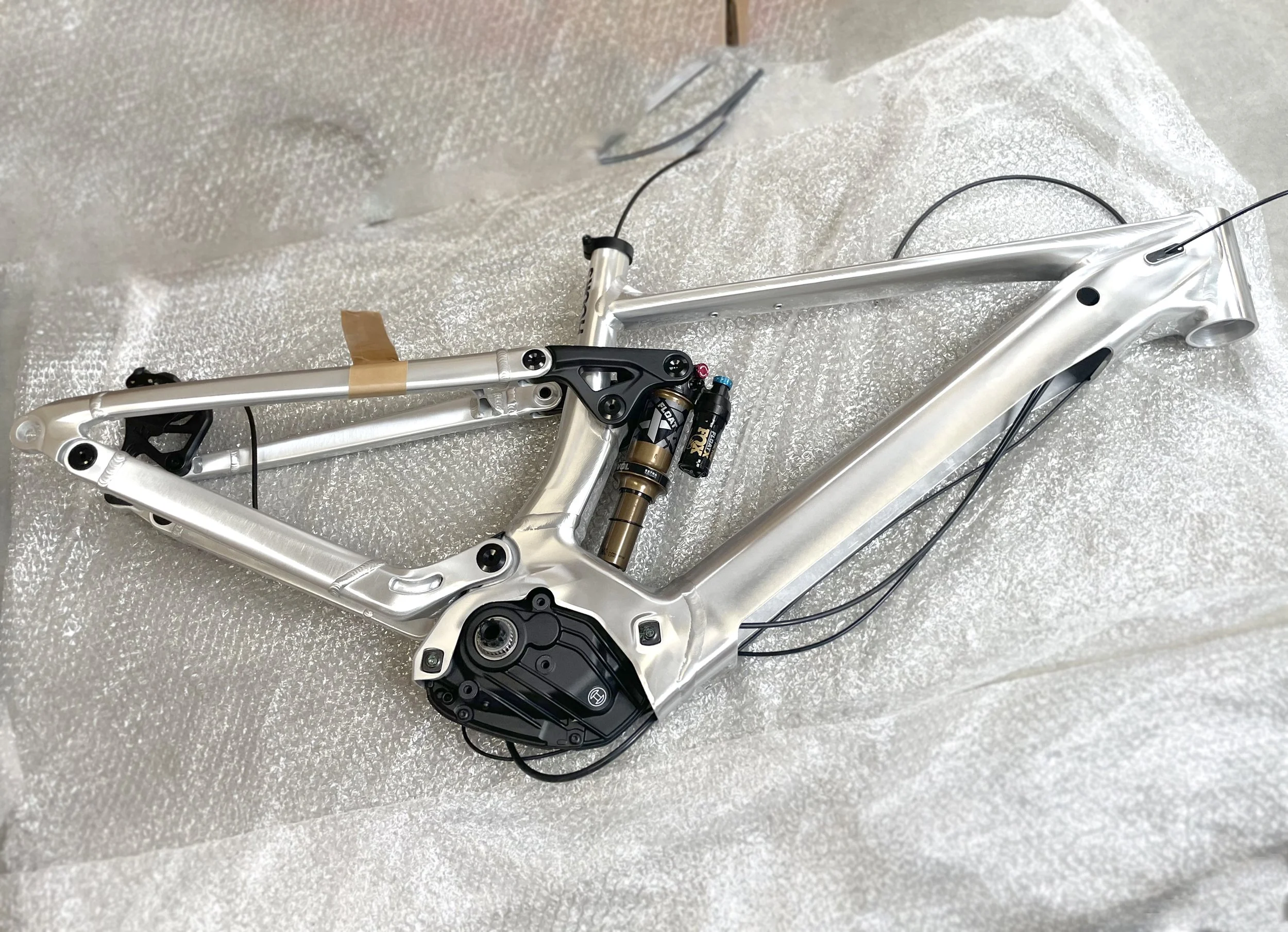 Cadre de vélo en aluminium avec suspension avant, fixations et câbles, posé sur du papier bulle