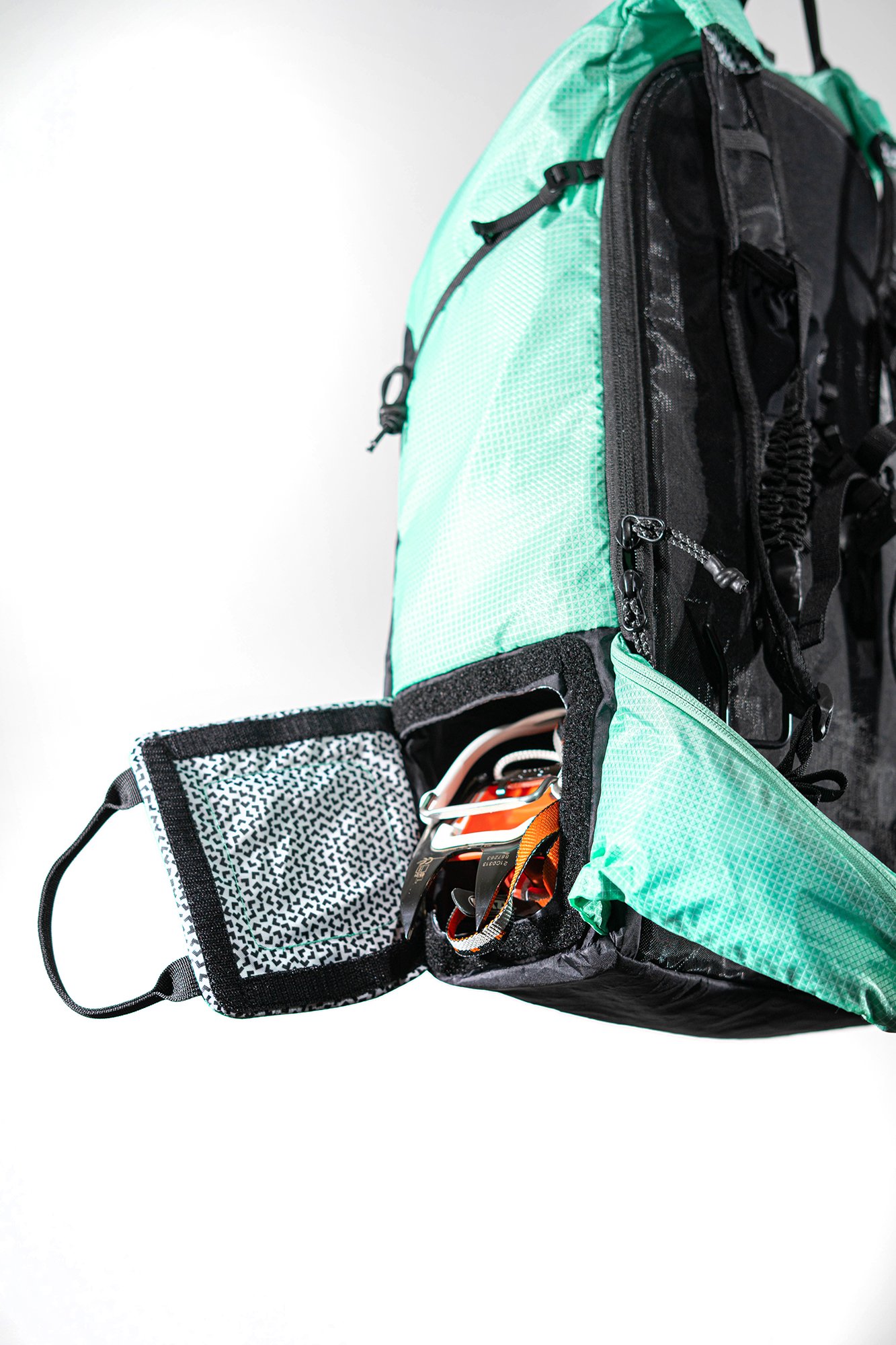 Un sac à dos de ski alpinisme de couleur cyan et noir Black Crows Dorsa 20, avec plusieurs compartiments, un filet élastique et des bretelles ajustables, contenant du matériel d'extérieur, sur un fond blanc.