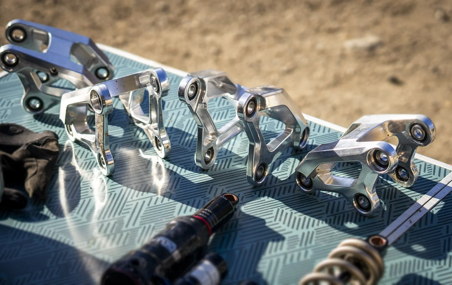 Multiple metallic bicycle or motorcycle component parts laid out on a patterned blue surface outdoors.