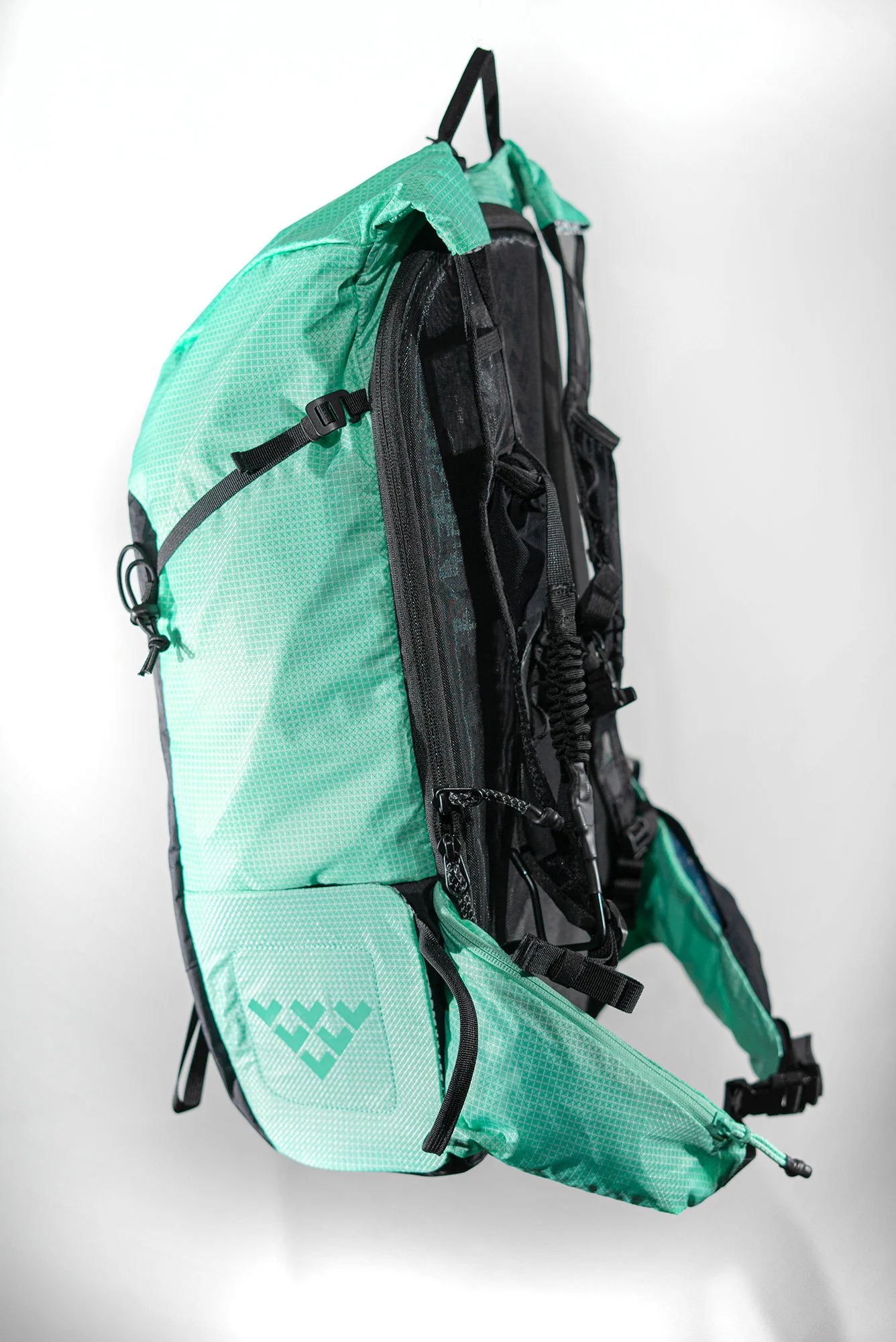 Un sac à dos de ski alpinisme de couleur cyan et noir Black Crows Dorsa 20, avec plusieurs compartiments, un filet élastique et des bretelles ajustables, contenant du matériel d'extérieur, sur un fond blanc.