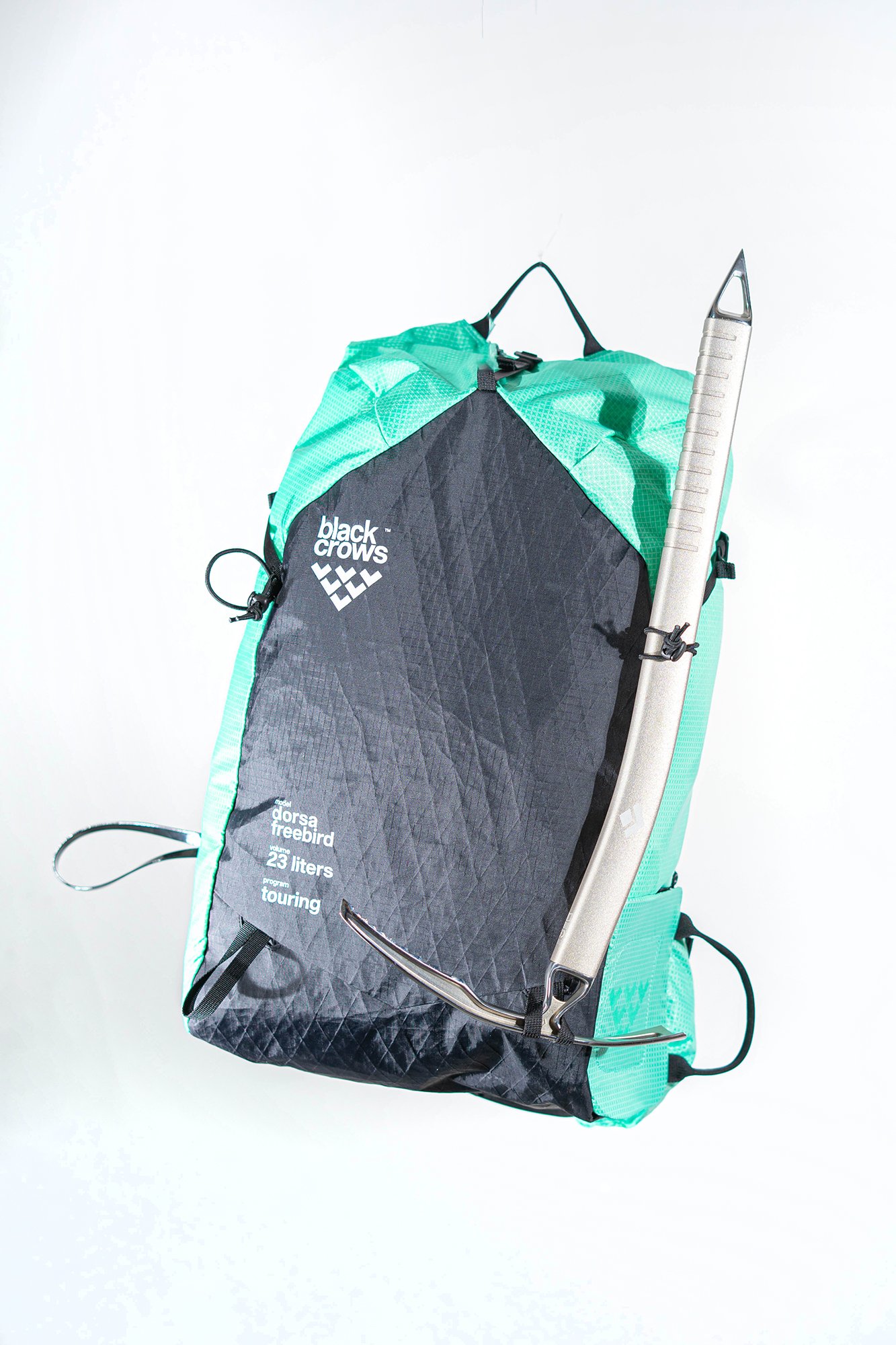 Un sac à dos de ski alpinisme de couleur cyan et noir Black Crows Dorsa 20, avec plusieurs compartiments, un filet élastique et des bretelles ajustables, contenant du matériel d'extérieur, sur un fond blanc.