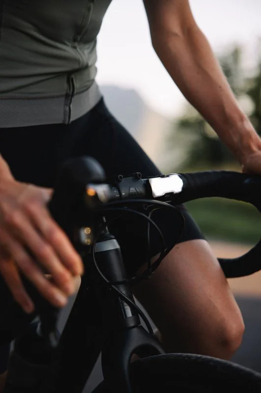 Partie inférieure d'une personne en pleine activité à vélo, portant un t-shirt gris et des vêtements de sport noirs, entourée d'un environnement en plein air.