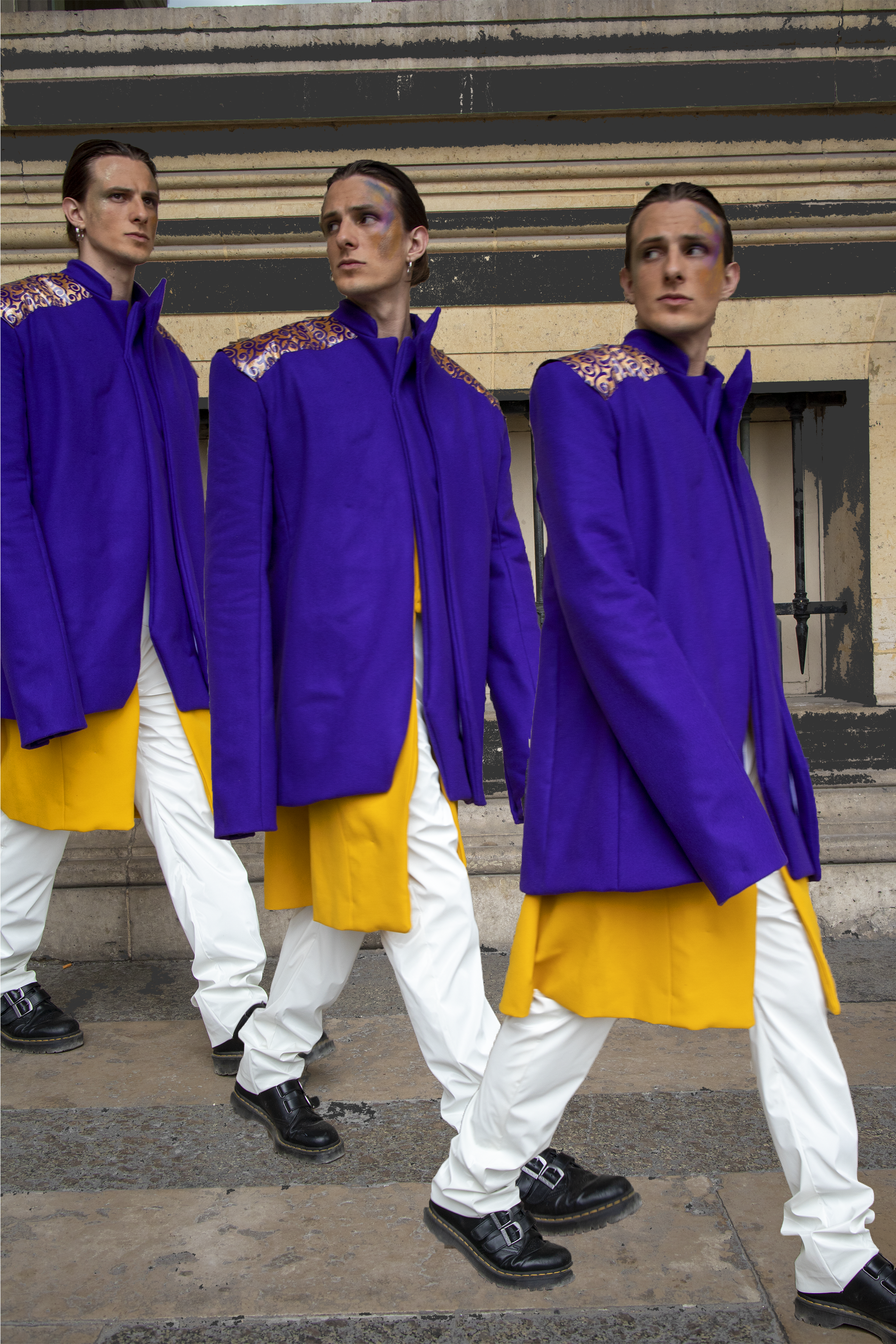 Trois personnes marchent côte à côte portant des manteaux violets avec des épaulettes dorées, des pantalons blancs et des bottes noires, en extérieur devant un bâtiment en pierre.