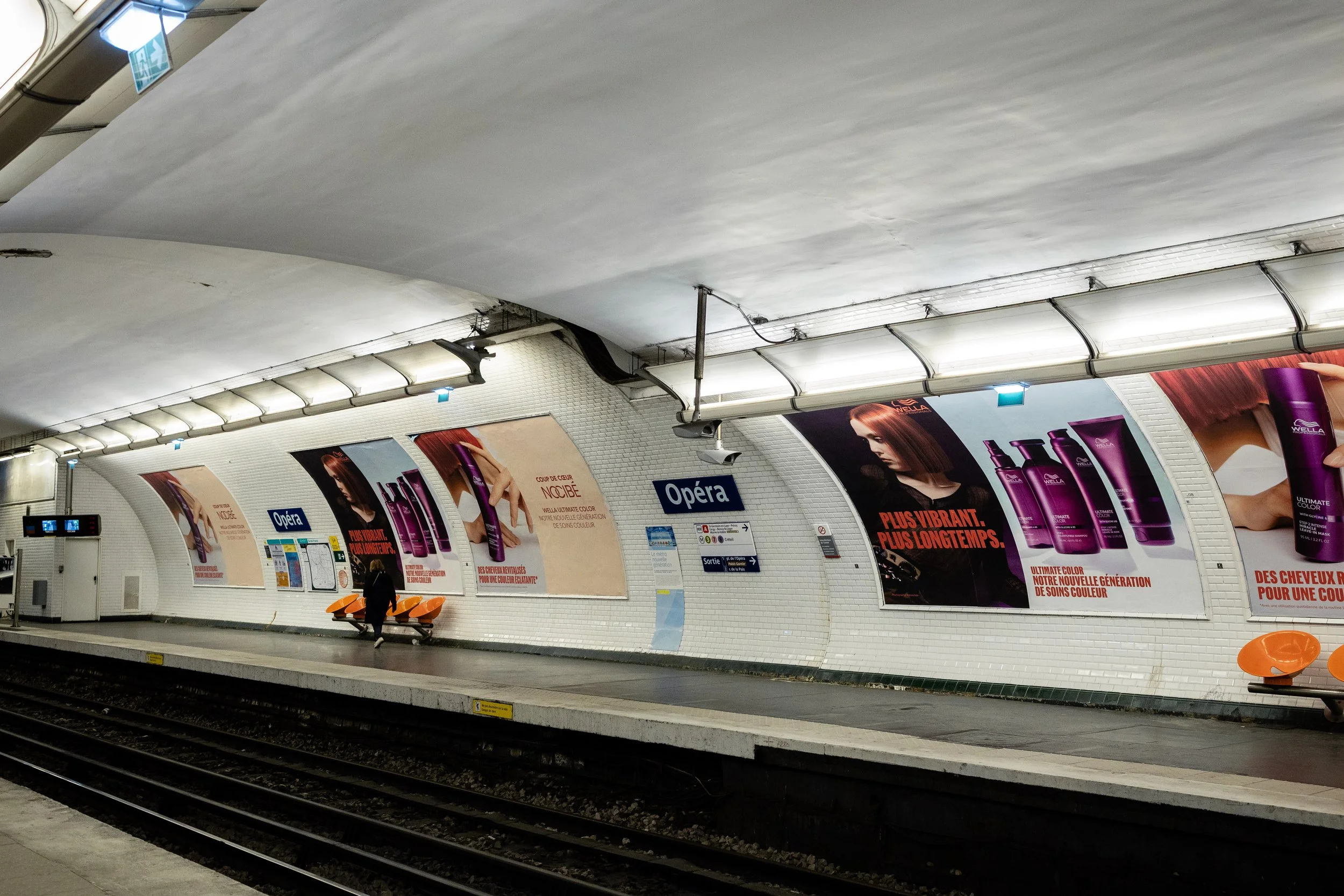 Publicités pour des produits capillaires dans une station de métro parisienne, avec une personne assise sur un banc.