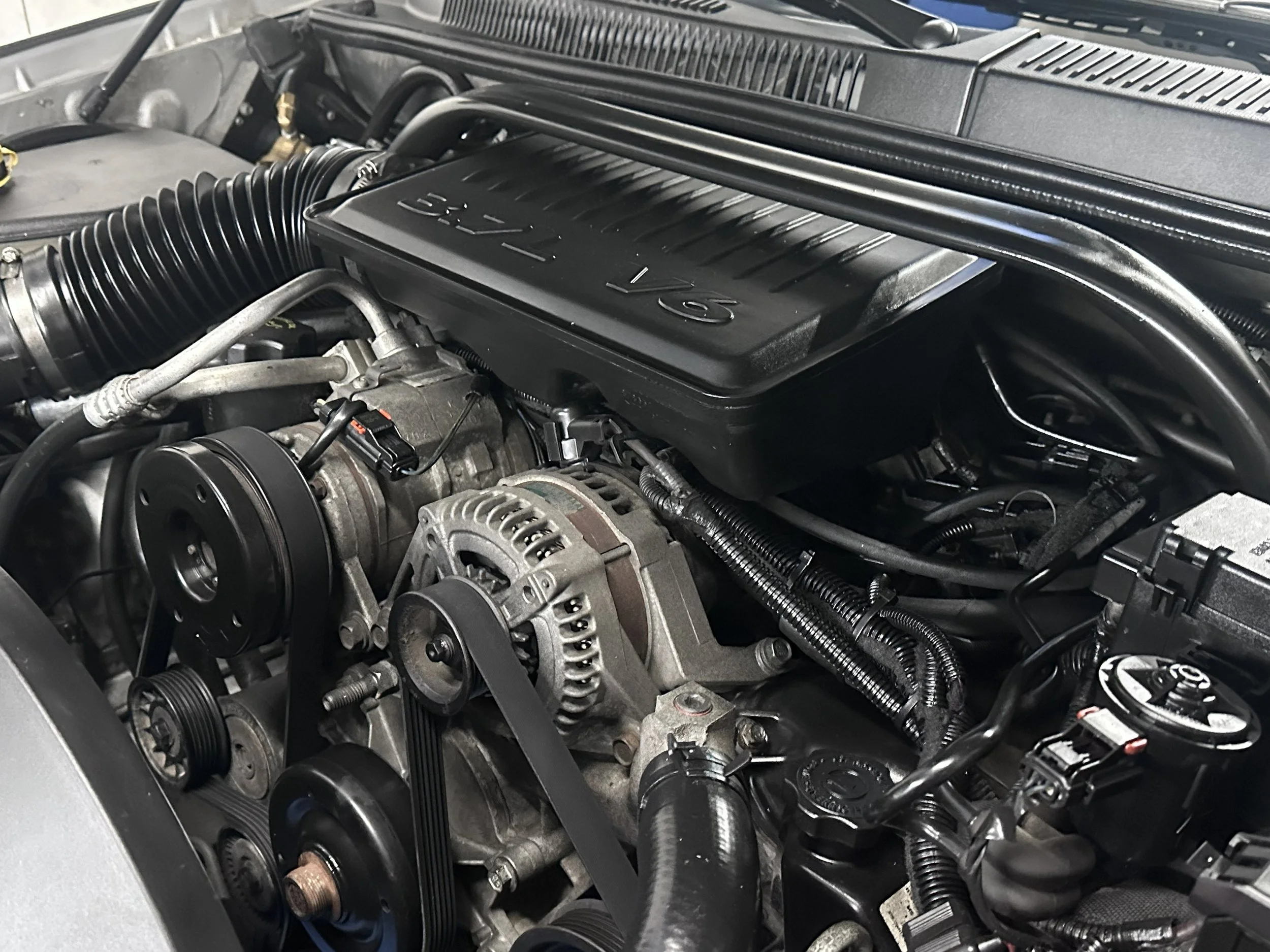 Close-up of a car engine with various belts, pulleys, and components visible under the hood.